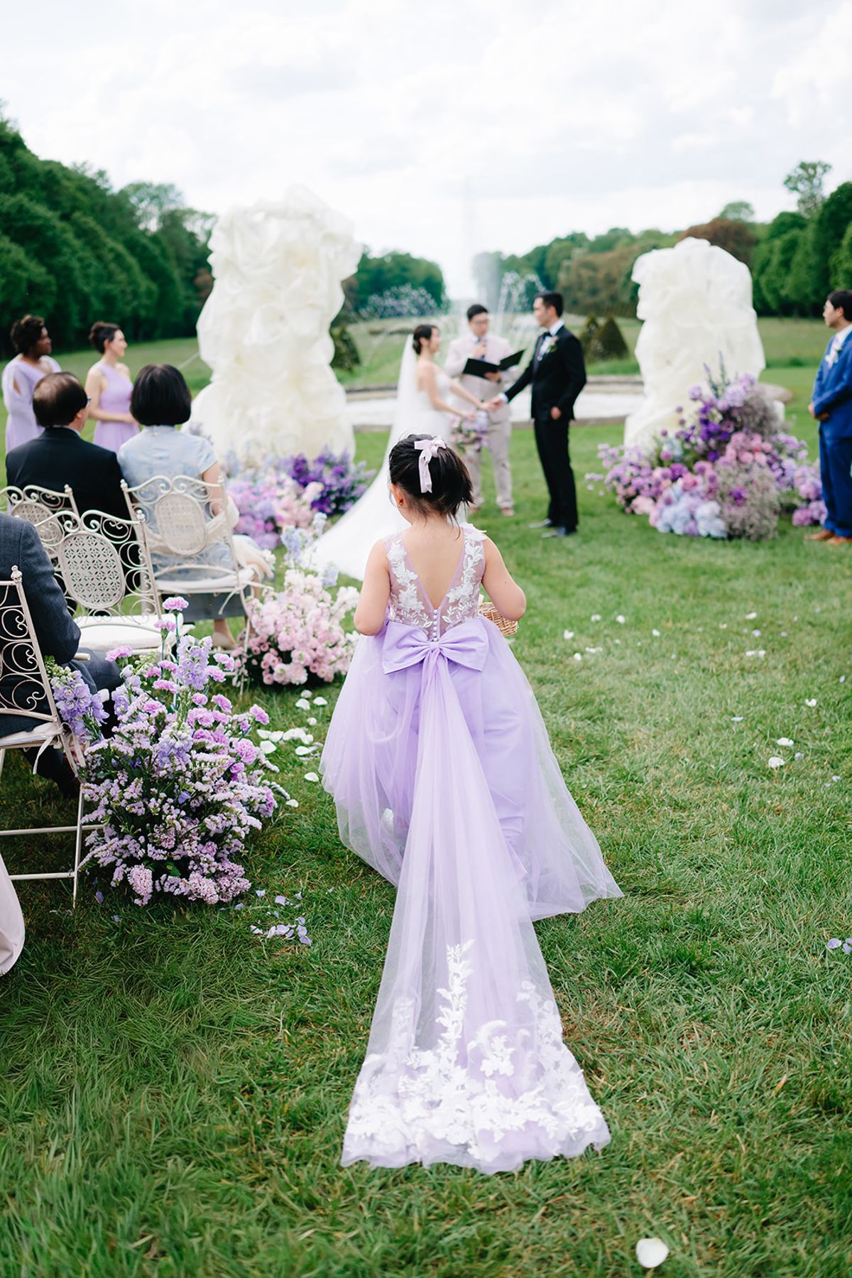 Liana and Ruiji walking the aisle with their flower girl in a lilac dress