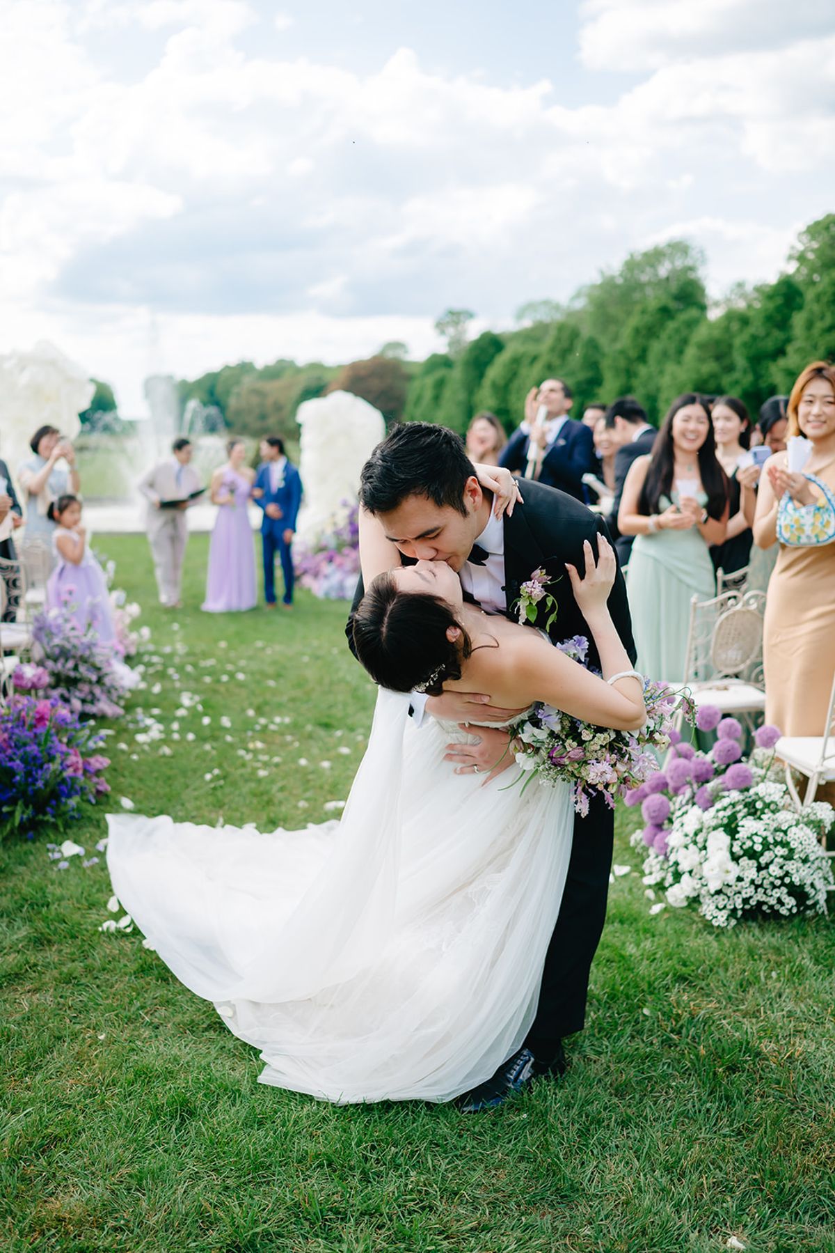 Liana and Ruiji embracing among the ceremony florals as guests look on