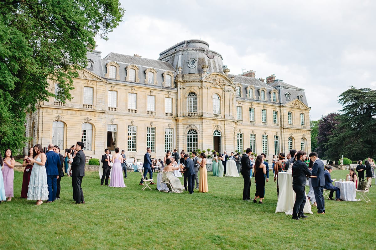 Guests mingling on the lawn in front of Château de Champlâtreux during cocktail hour