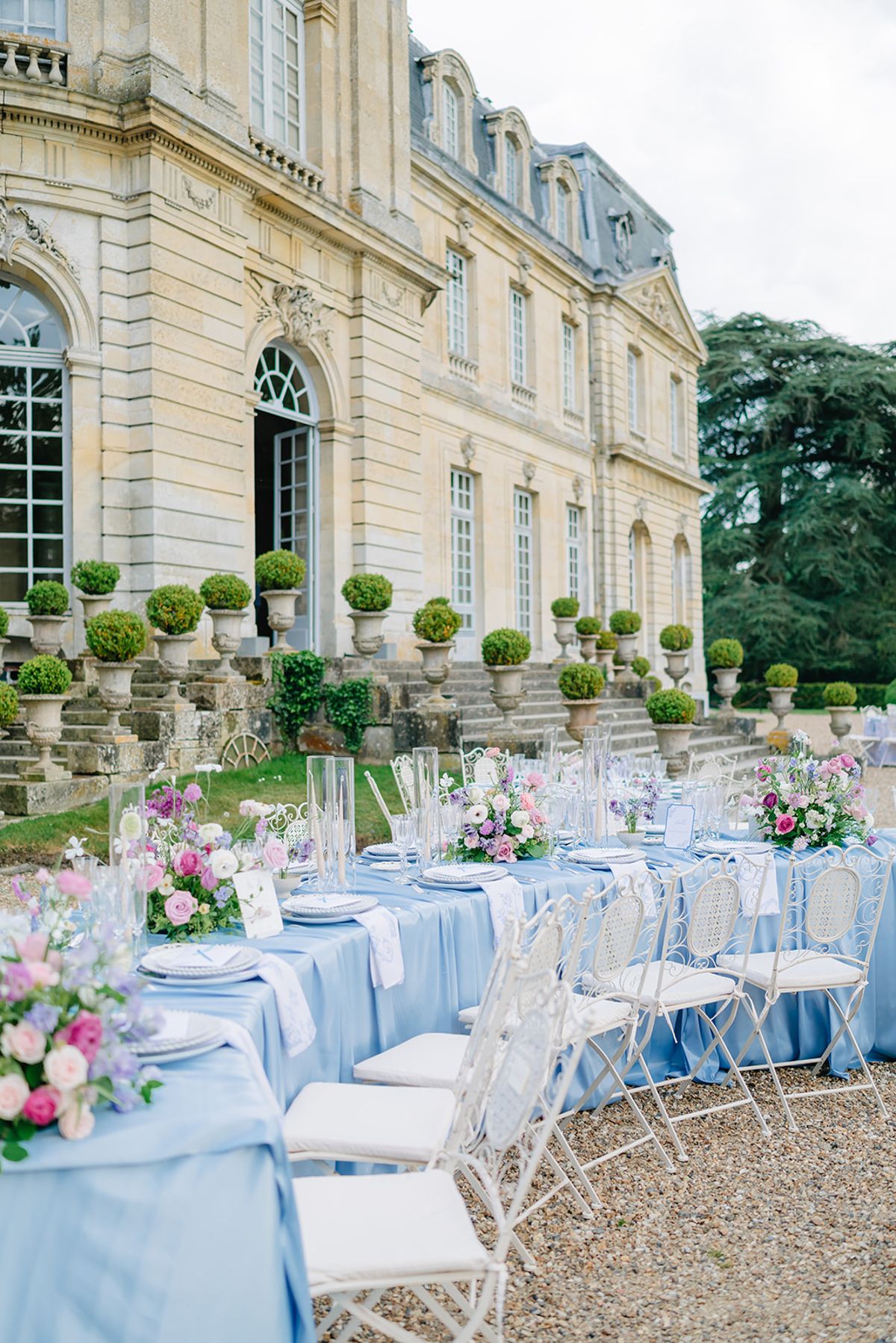Round reception tables in blue linen set out in front of Château de Champlâtreux
