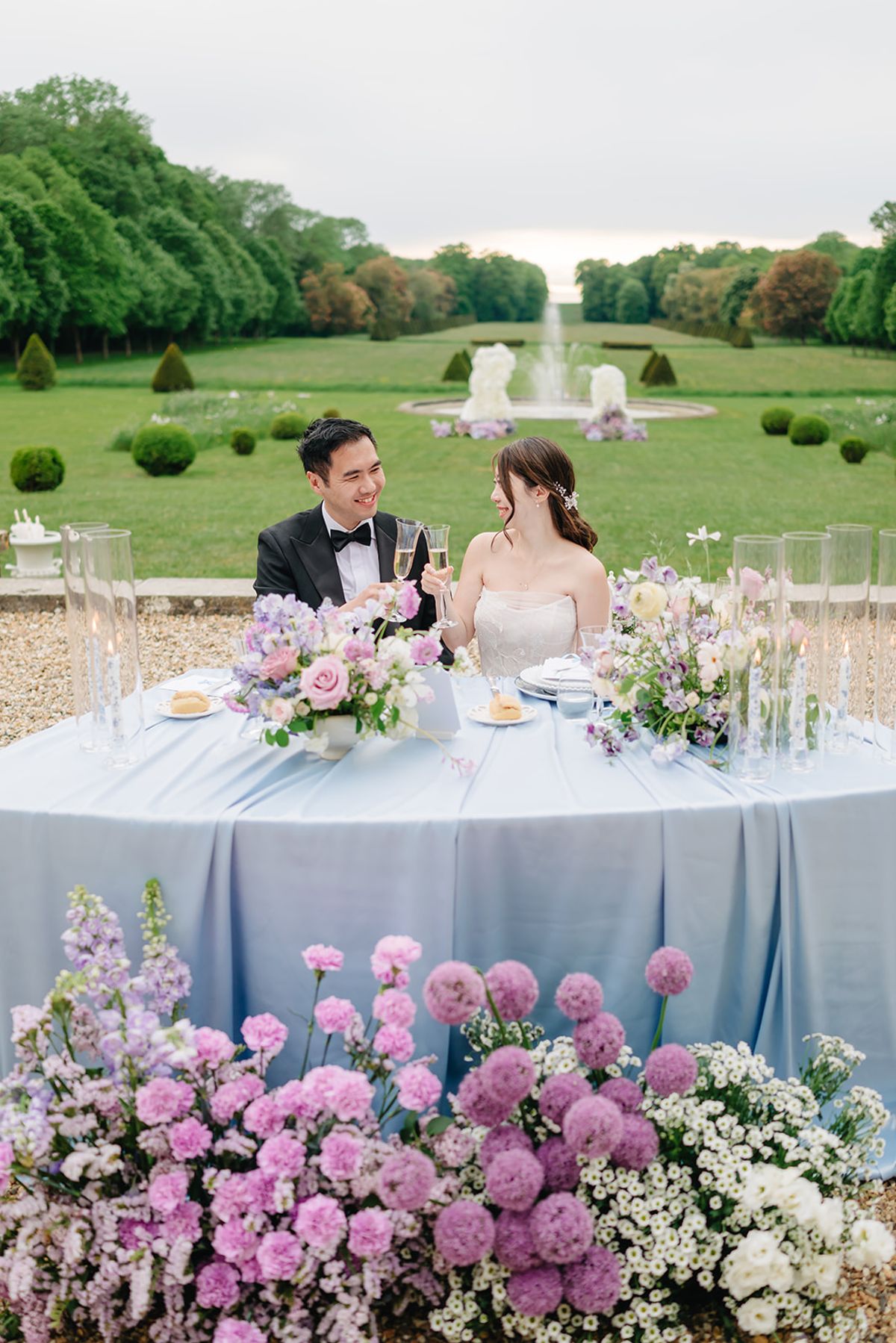 Liana and Ruiji seated together at their reception table in blue linens
