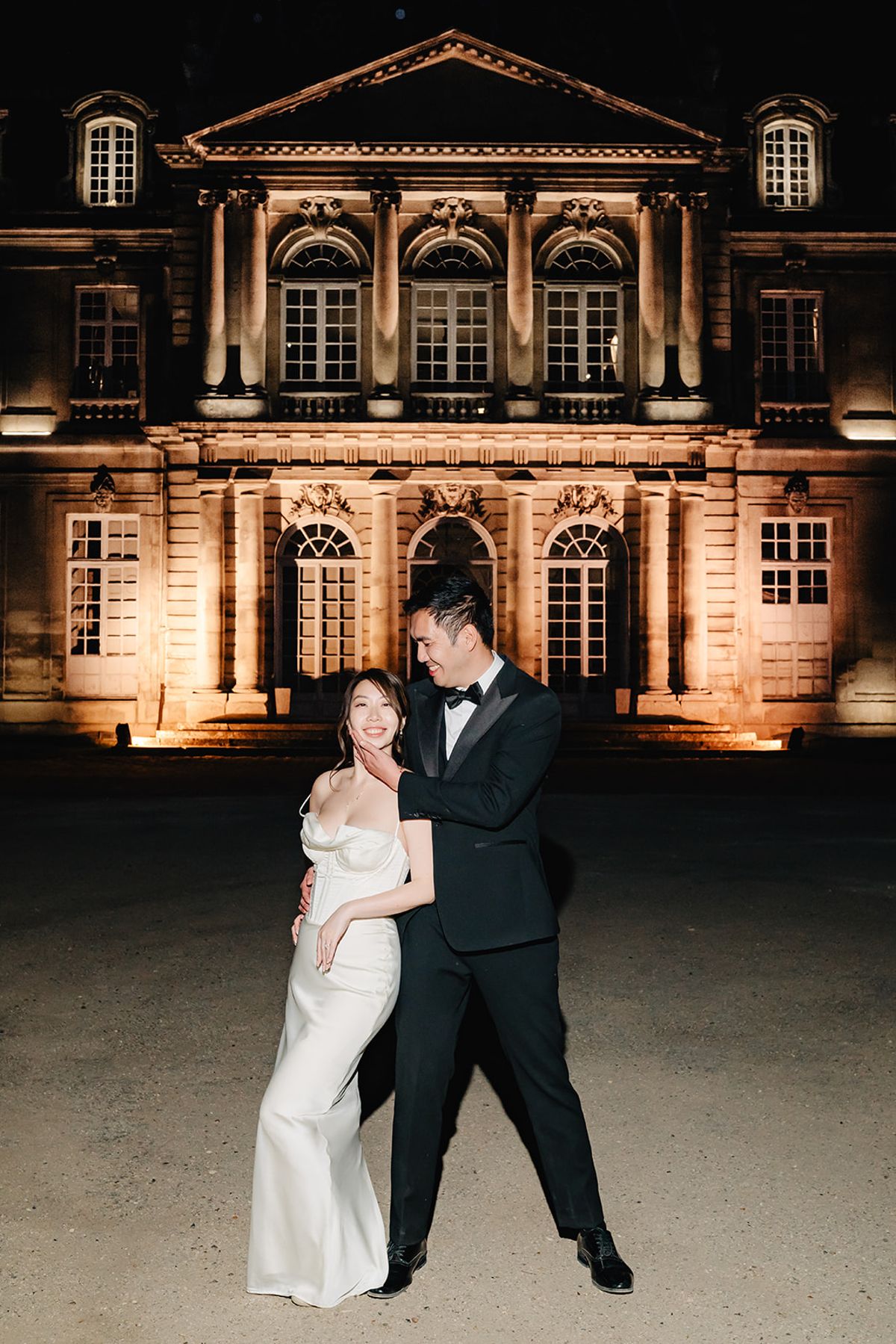 Liana and Ruiji posed at night in front of the illuminated Château de Champlâtreux