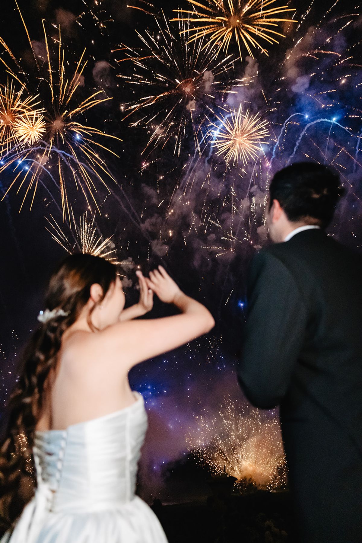 Liana and Ruiji silhouetted against fireworks over the Château de Champlâtreux grounds