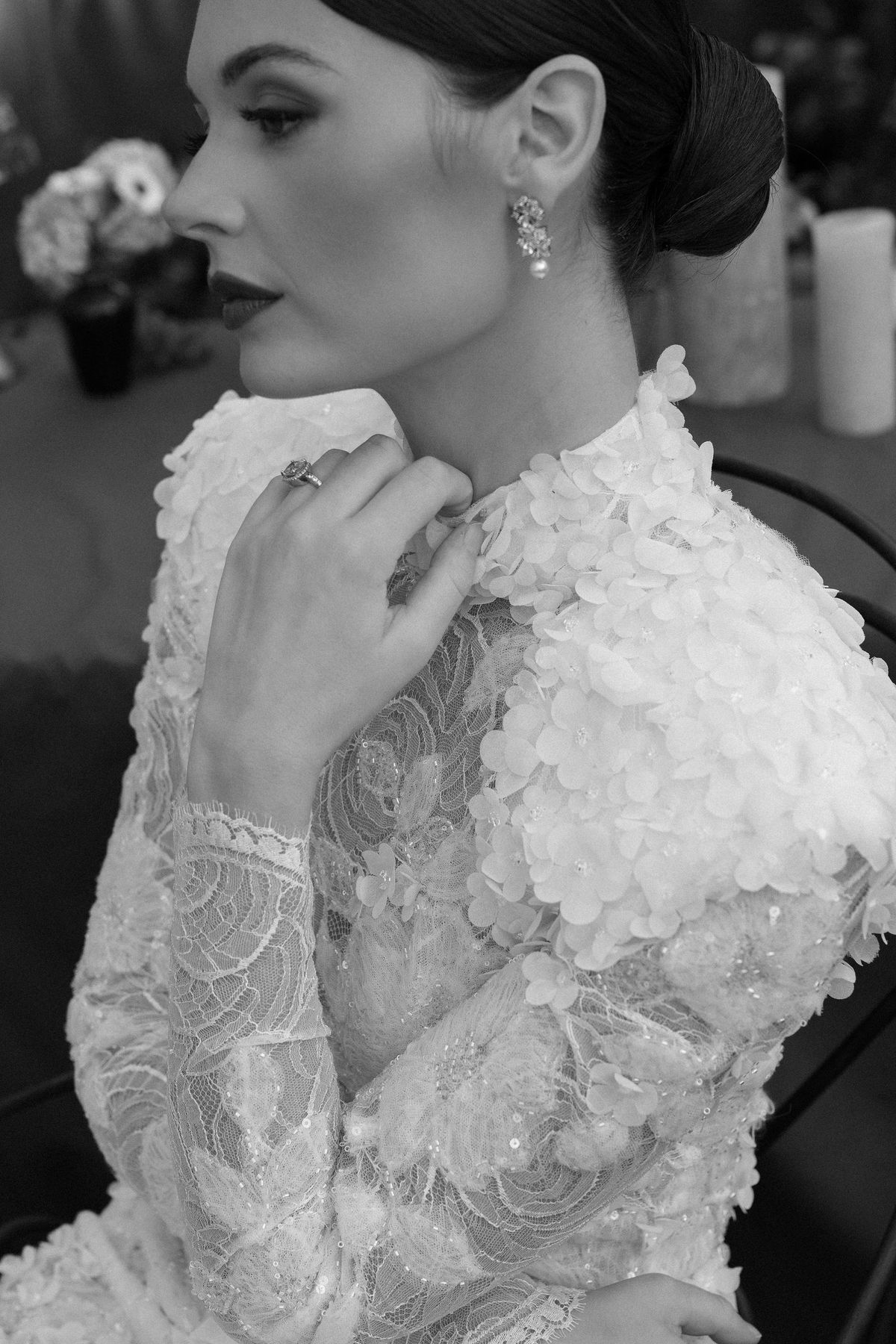 A black and white profile of the bride in drop earrings and a lace gown, with her hand raised to her collar.
