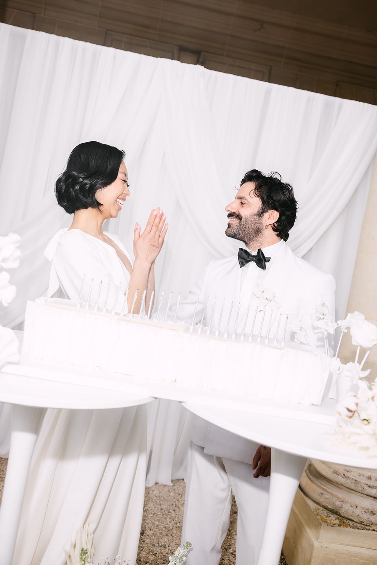 Bride clapping and laughing with the groom across a long white candle-topped cake