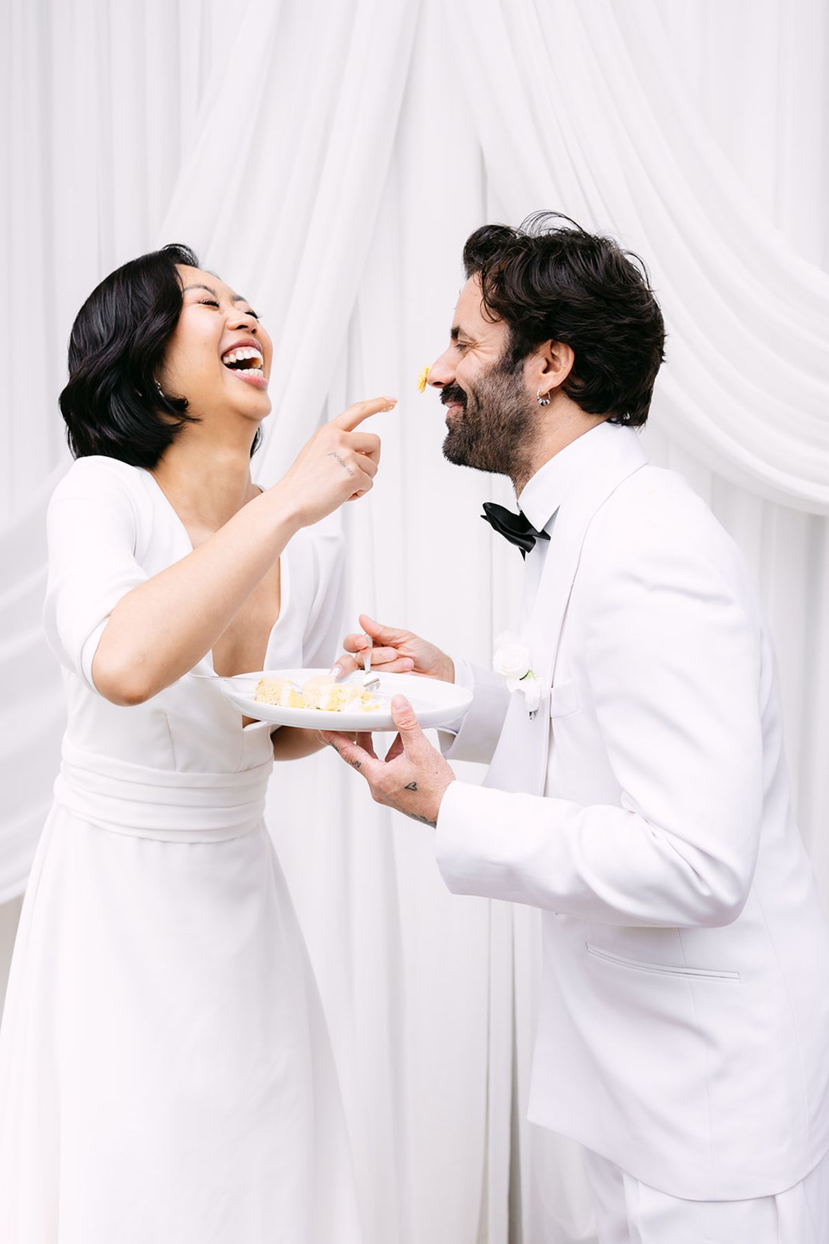 Bride laughing as she dabs cake on the groom's nose