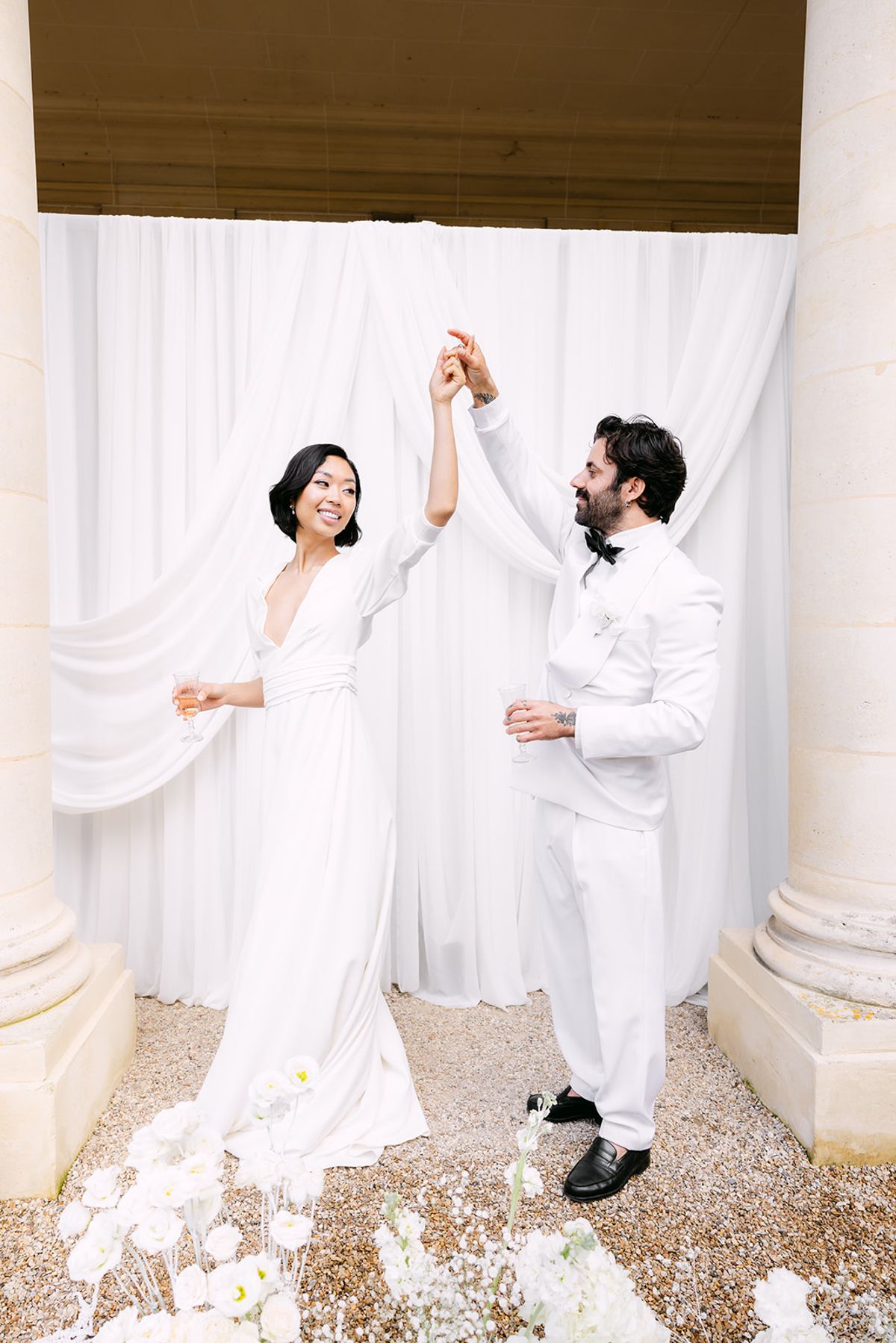 Groom twirling the bride in front of draped white fabric between stone columns