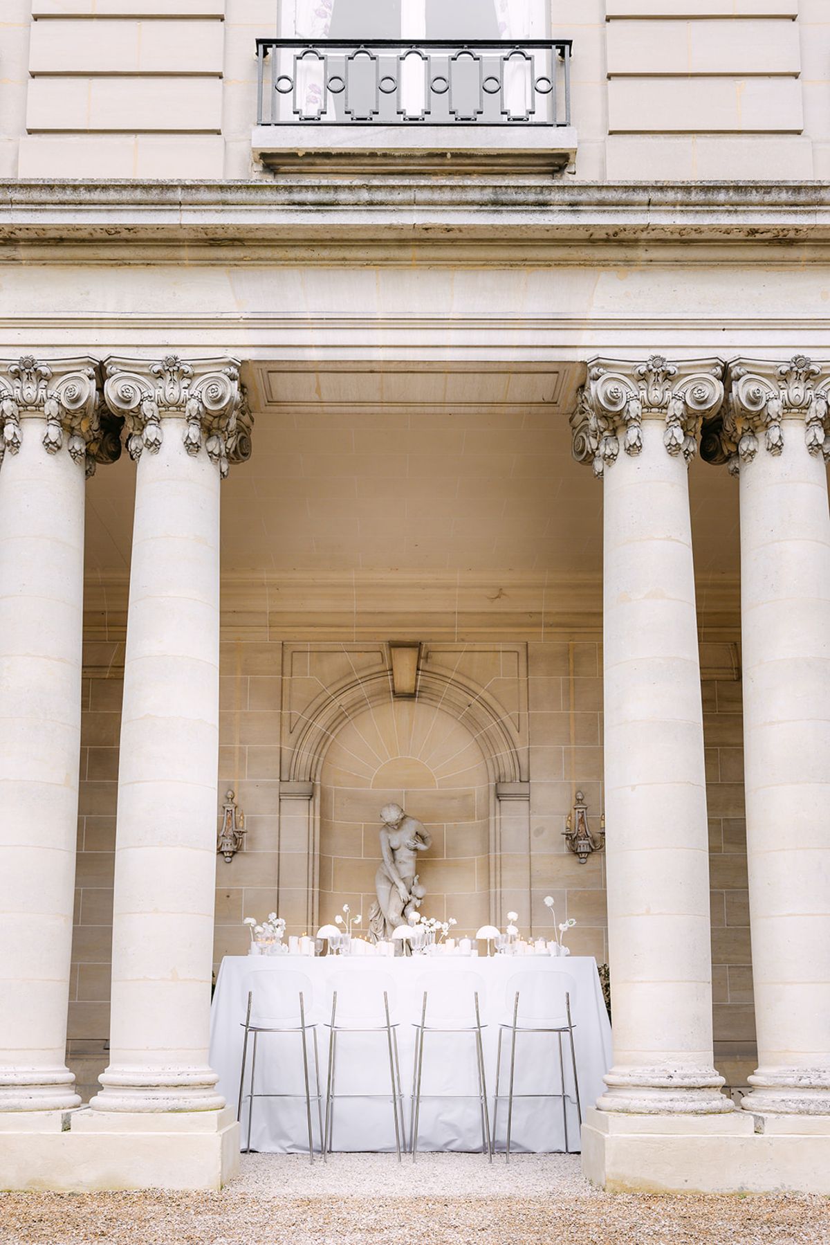 Dinner table set beneath the carved niche and Corinthian columns of the stone colonnade at Château du Prieuré d'Évecquemont