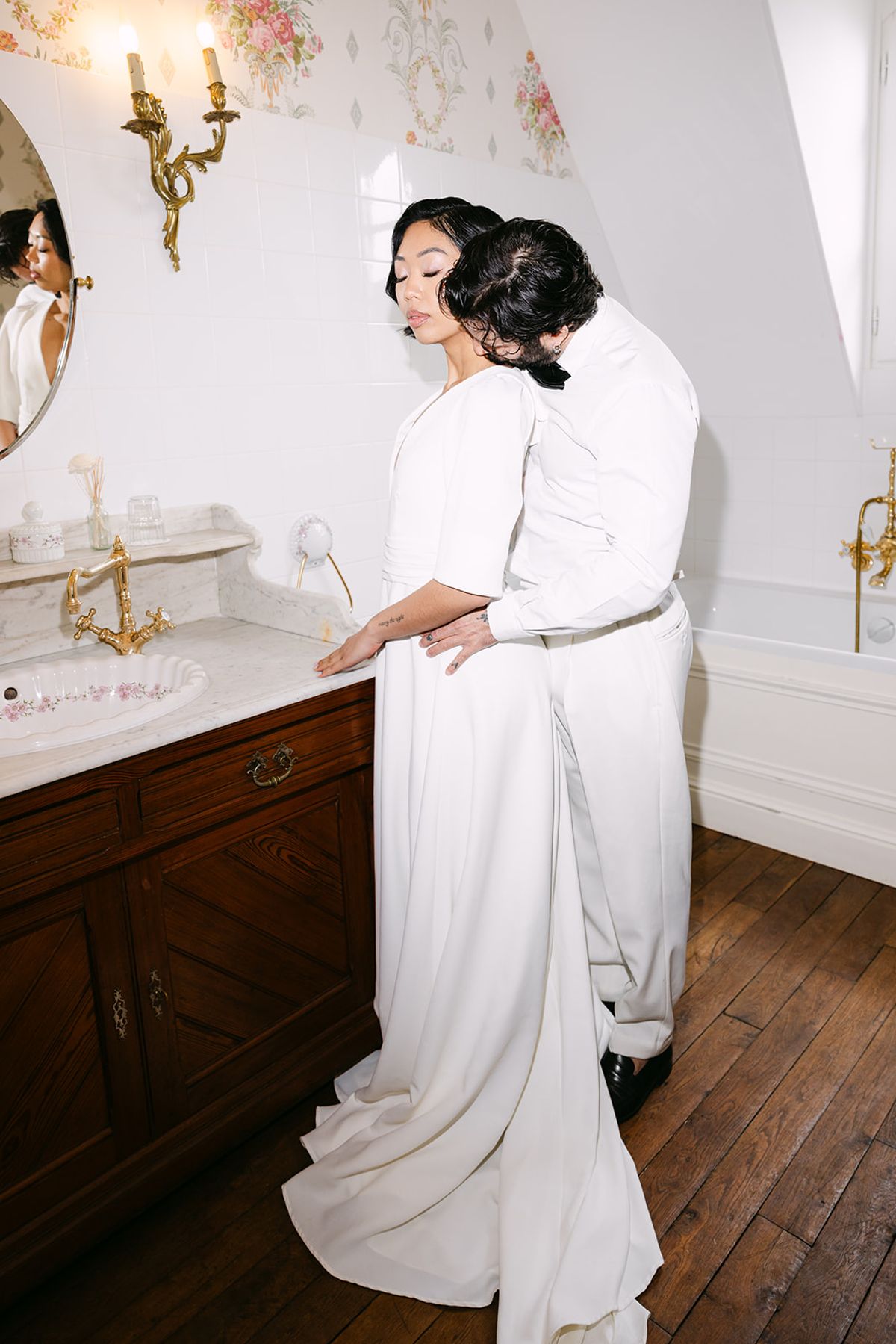 Groom kissing the bride's neck at a marble washstand with gilt taps in a bathroom at Château du Prieuré d'Évecquemont