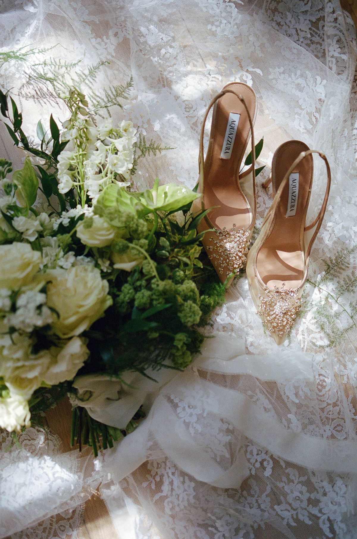 Beaded heels and a white bouquet arranged on a bed of greenery, shot on film