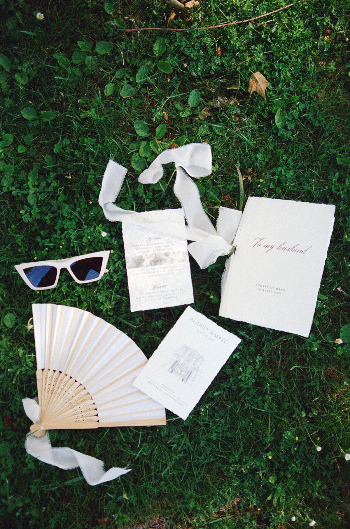 Wedding stationery, sunglasses and a folding fan styled on grass