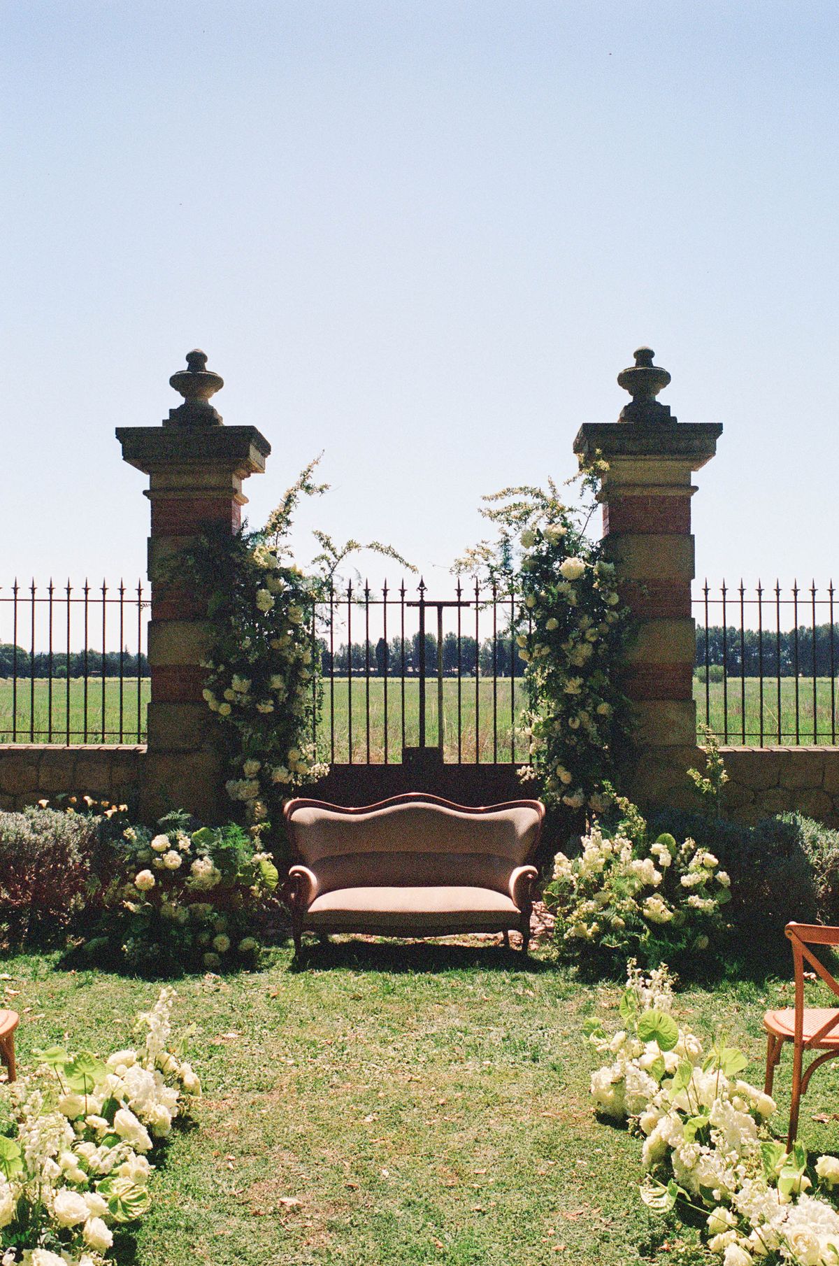 Wide view of the stone ceremony gateway wrapped in white florals, shot on film