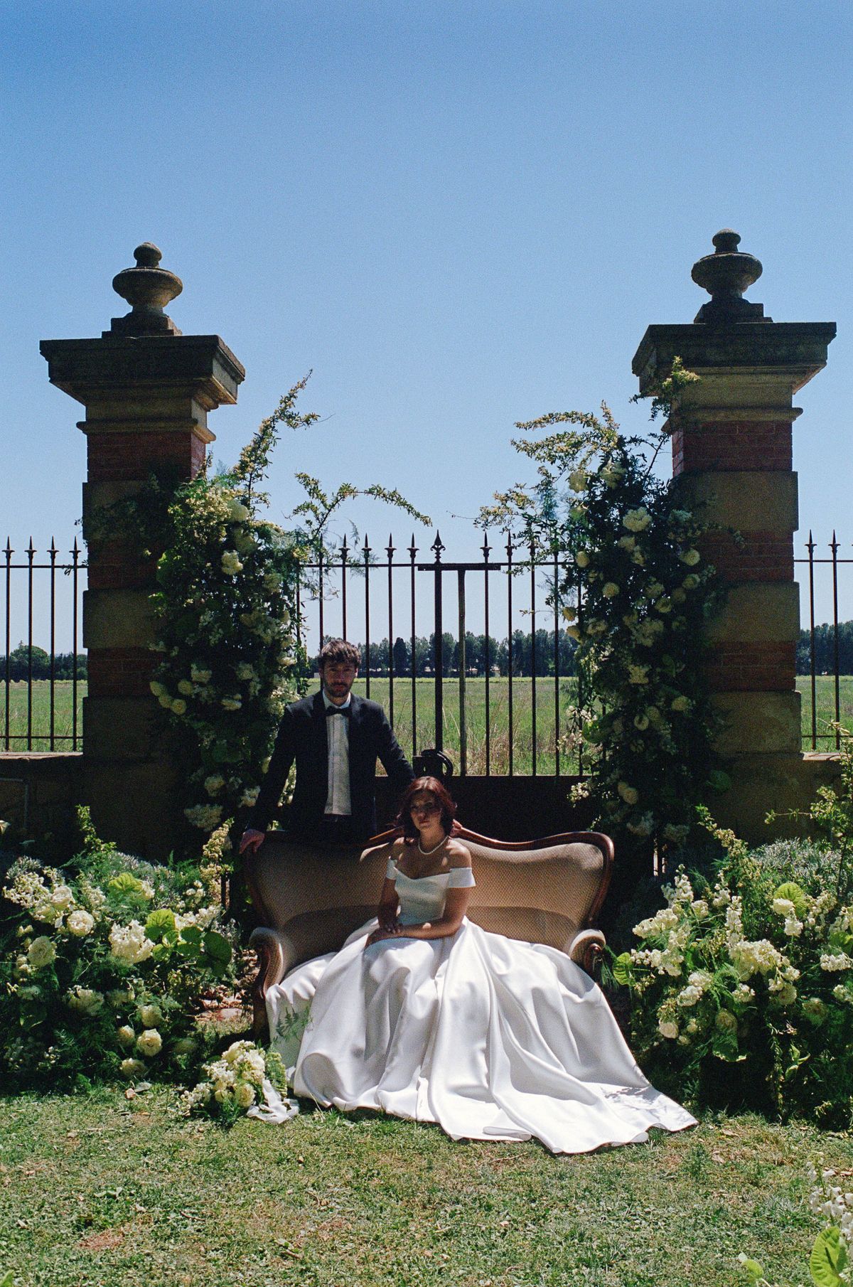 Wide film shot of the celebrant and couple seated at the stone archway ceremony setting