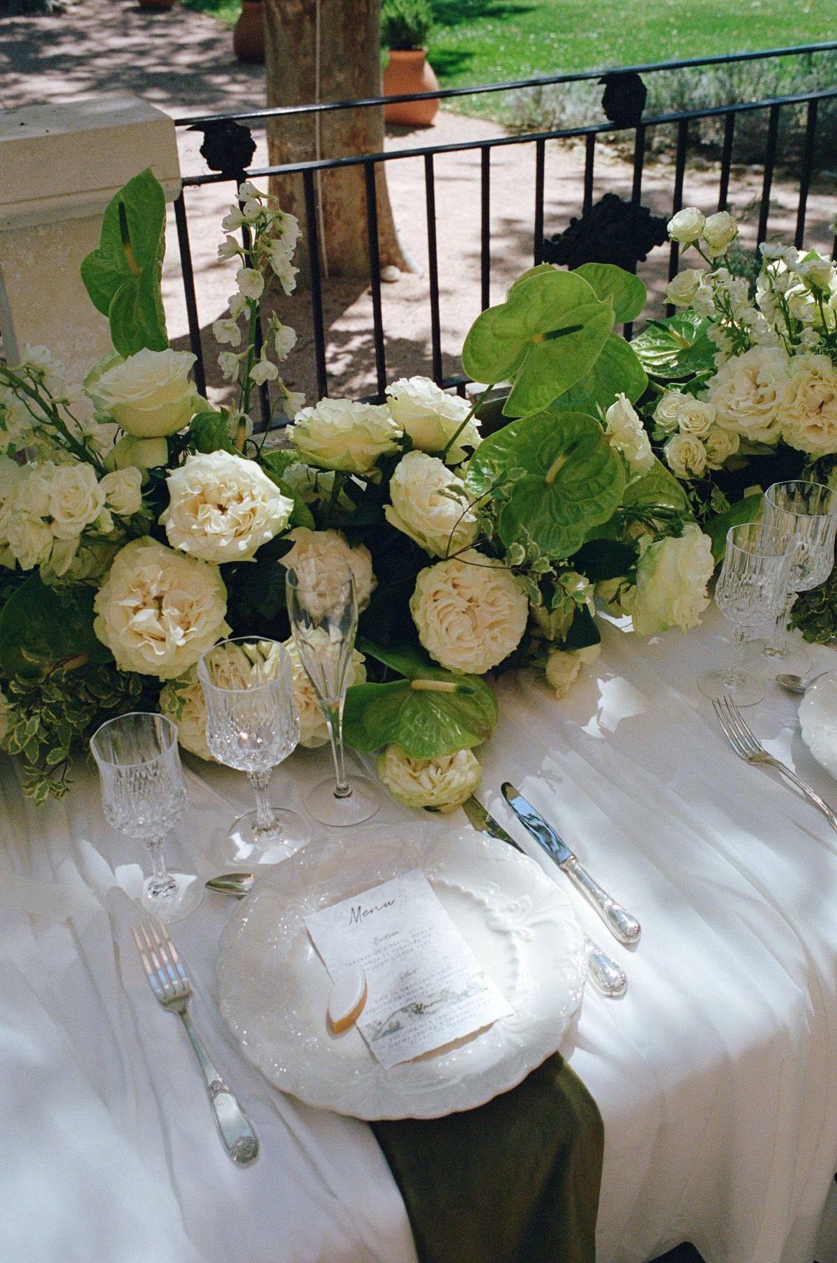 White rose centrepiece on the reception table beside crystal wine glasses, shot on film