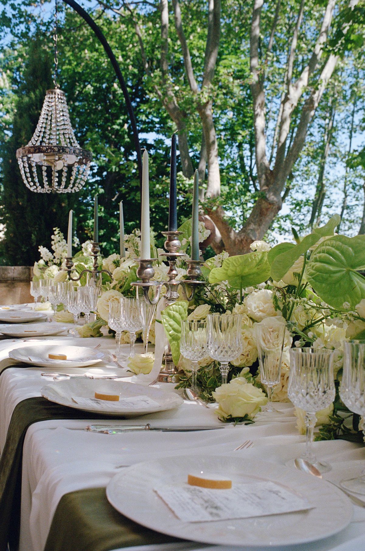Long outdoor reception table beneath trees, dressed with candelabra and white florals, shot on film