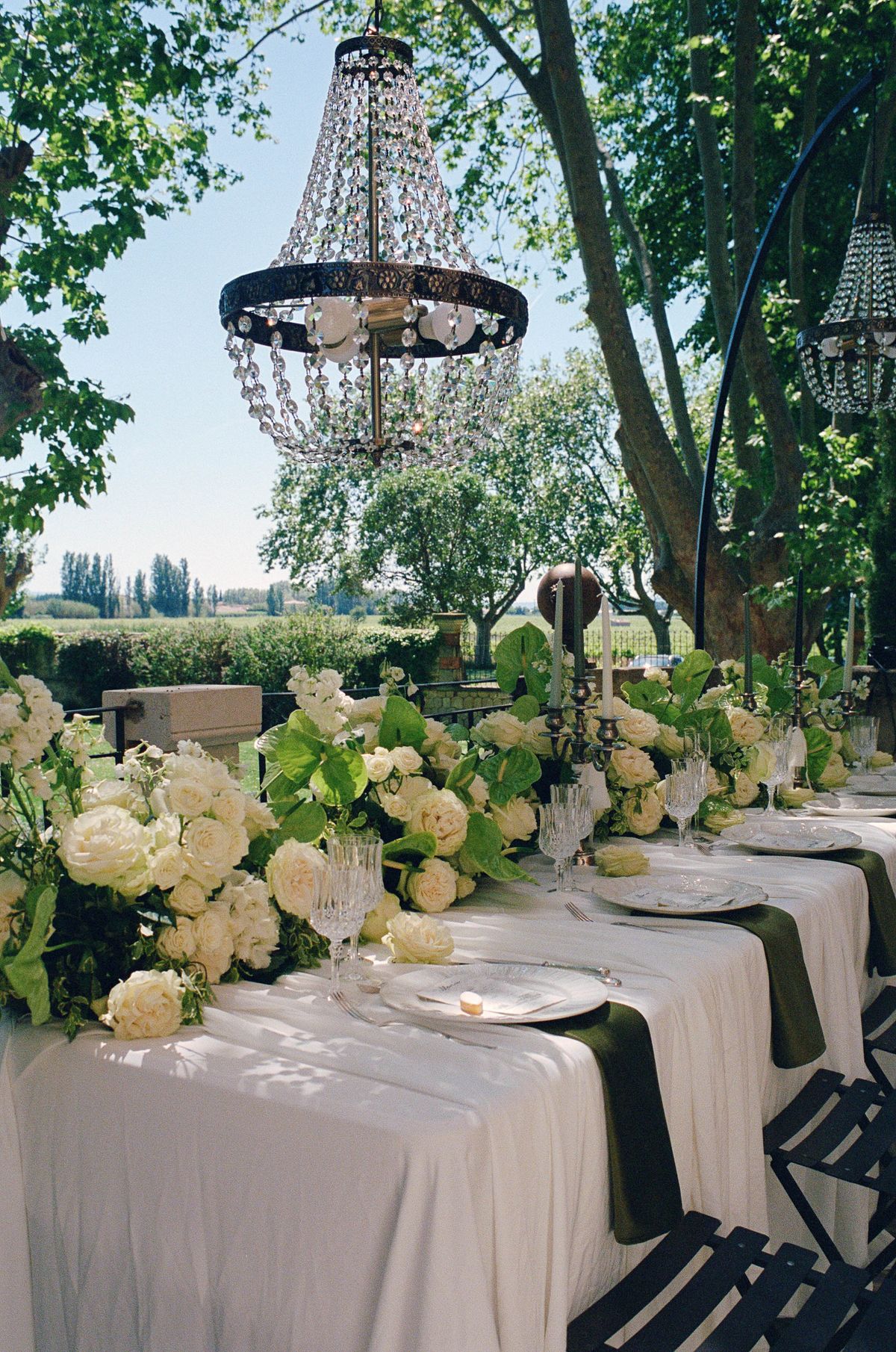 Long table dressed with white florals beneath trees, shot on film