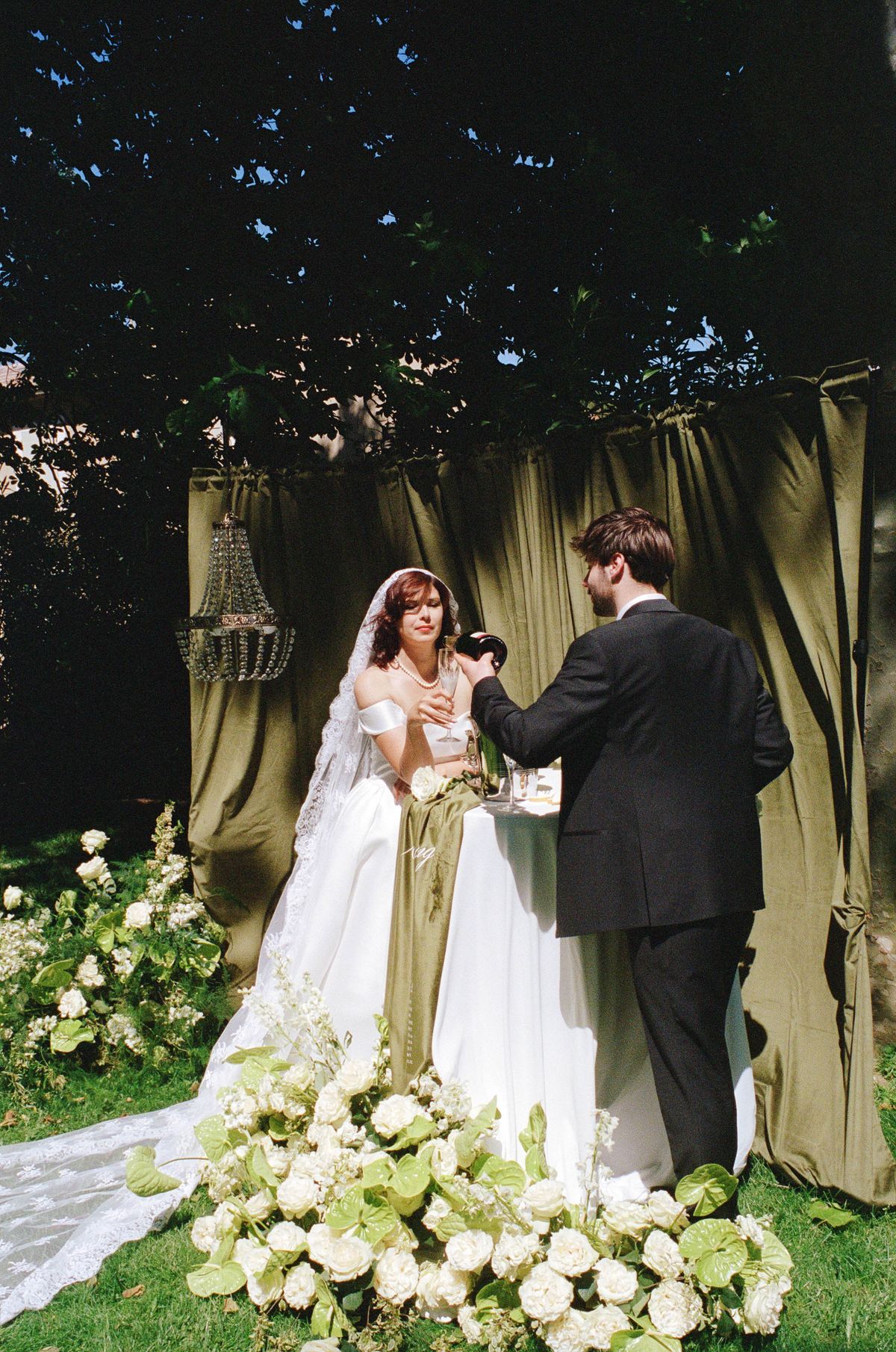 Bride and groom facing each other beneath a draped ceremony backdrop with hanging chandeliers
