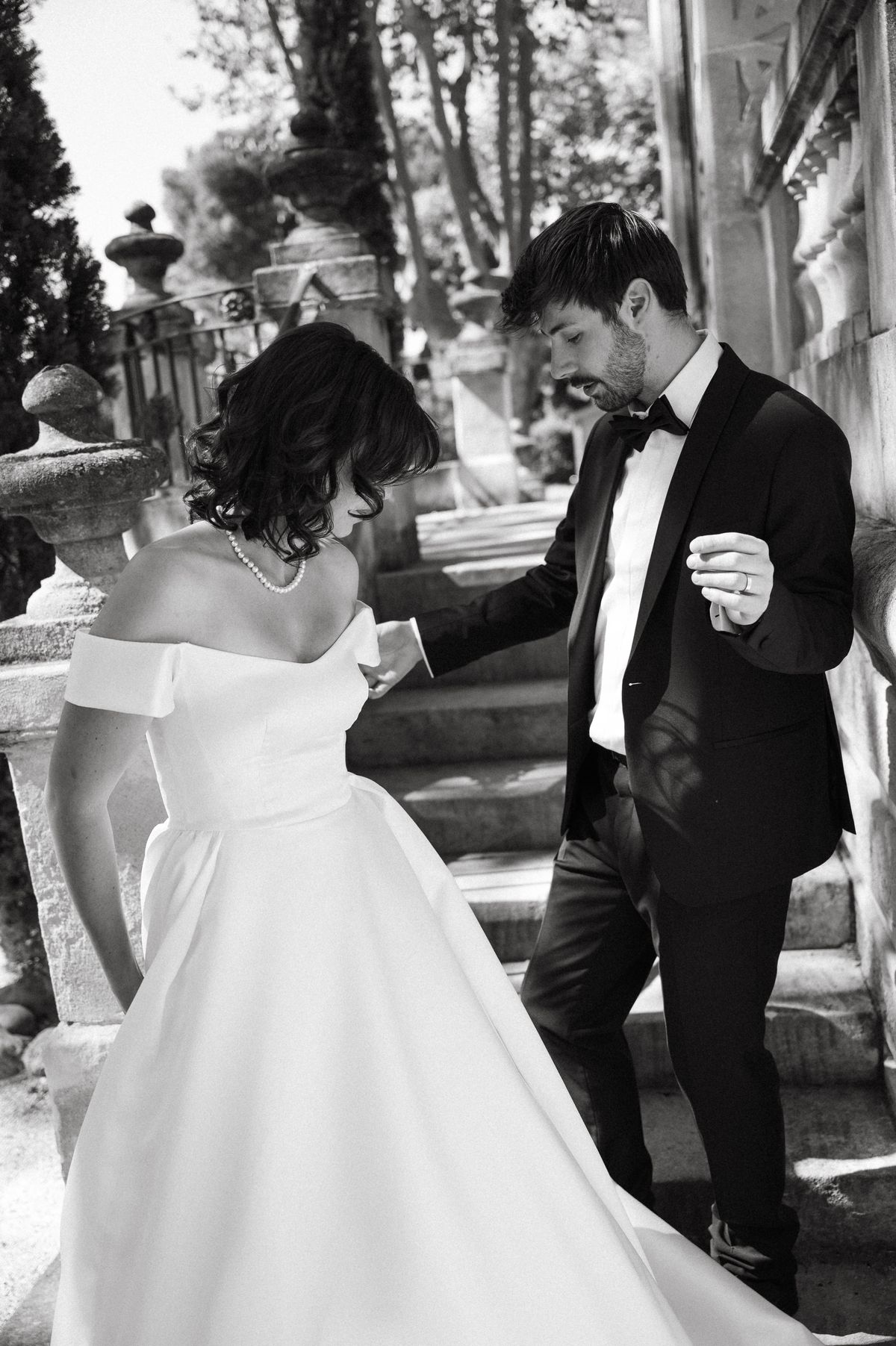 Black-and-white image of the couple descending the staircase, the bride's off-shoulder gown in detail