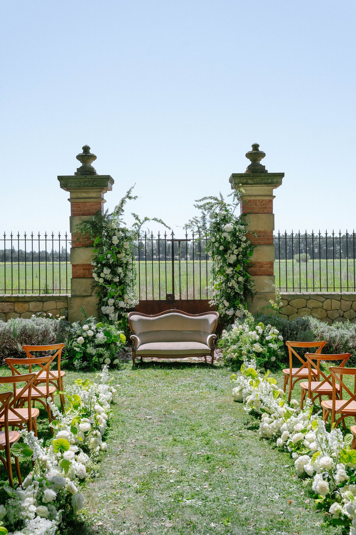 The stone ceremony gateway with an antique loveseat positioned beneath it, empty before the ceremony