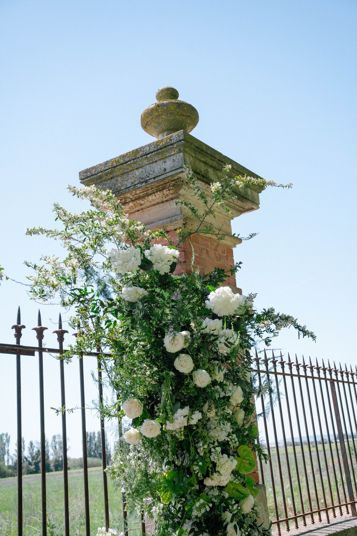 The stone pillar gateway framed by climbing white floral garlands against a clear sky