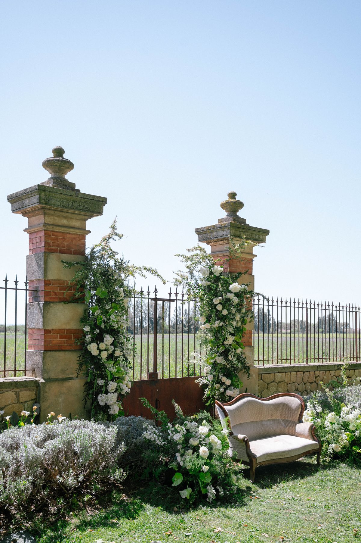 Stone pillar gateway dressed with climbing white floral garlands, open countryside beyond