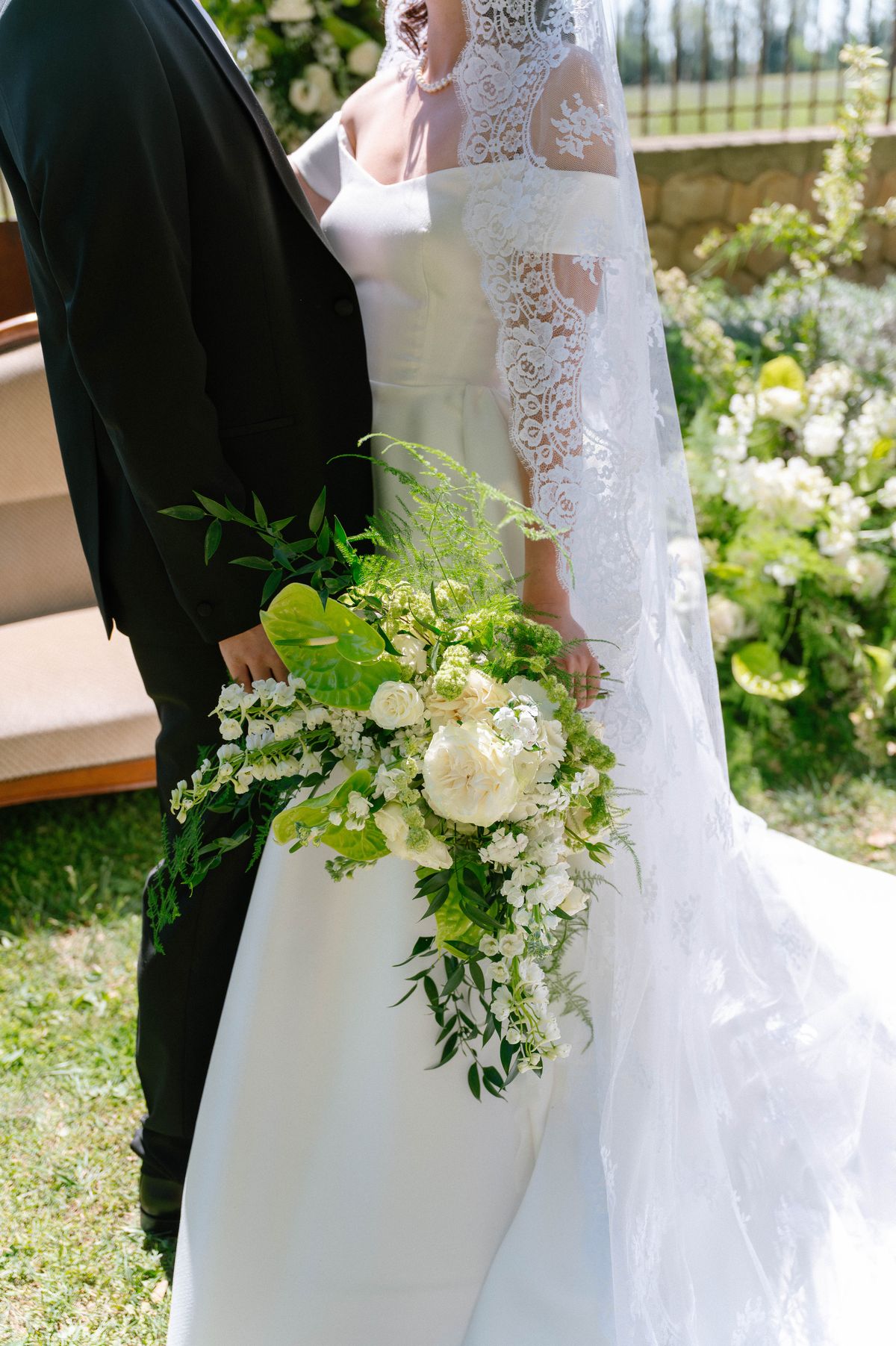 Close detail of the bride's bouquet and lace gown against the groom's tailored sleeve