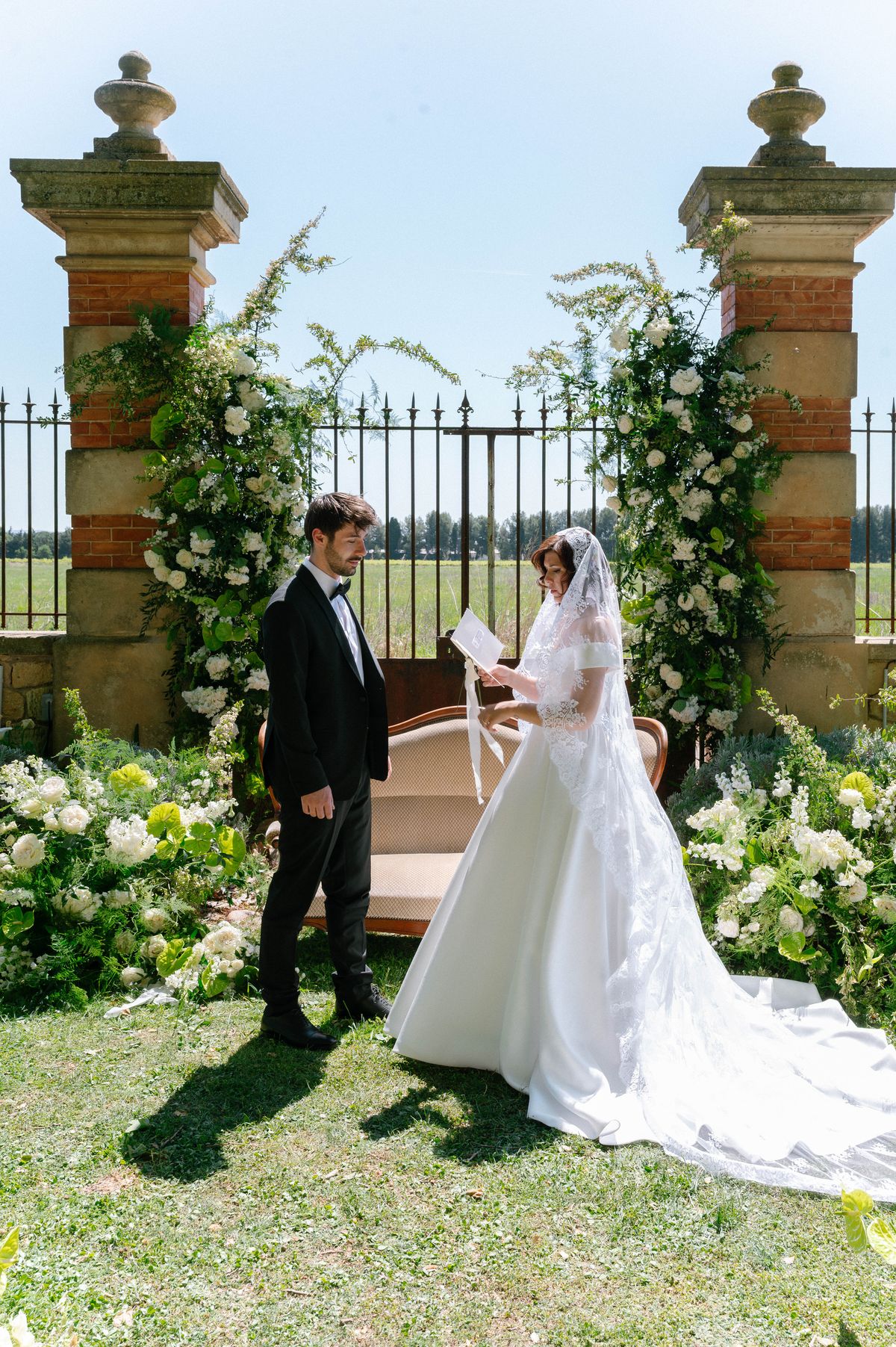 Groom reading his vows to the bride beneath the floral-dressed stone archway
