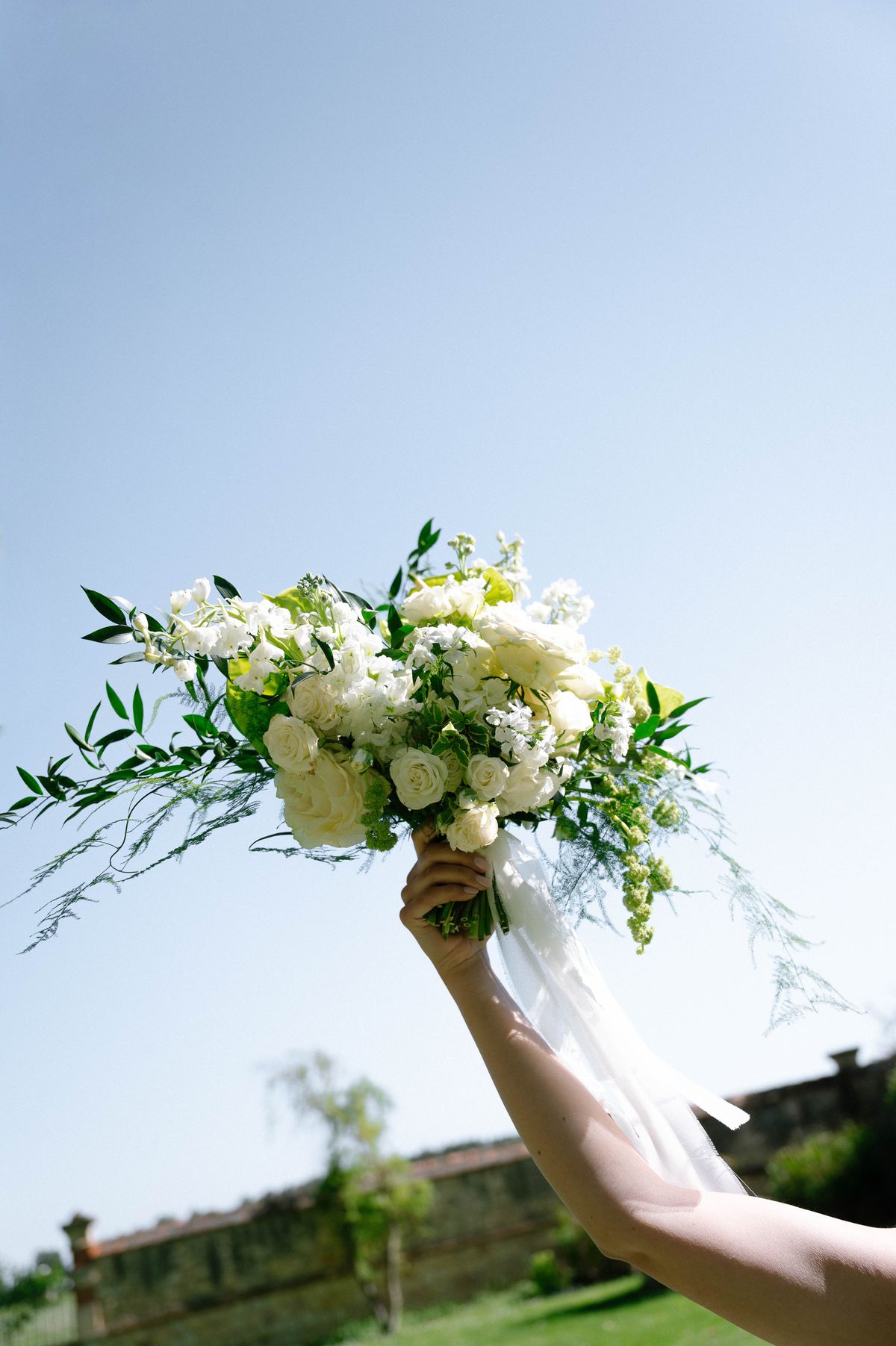 Bridal bouquet of white roses and trailing greenery held by hand