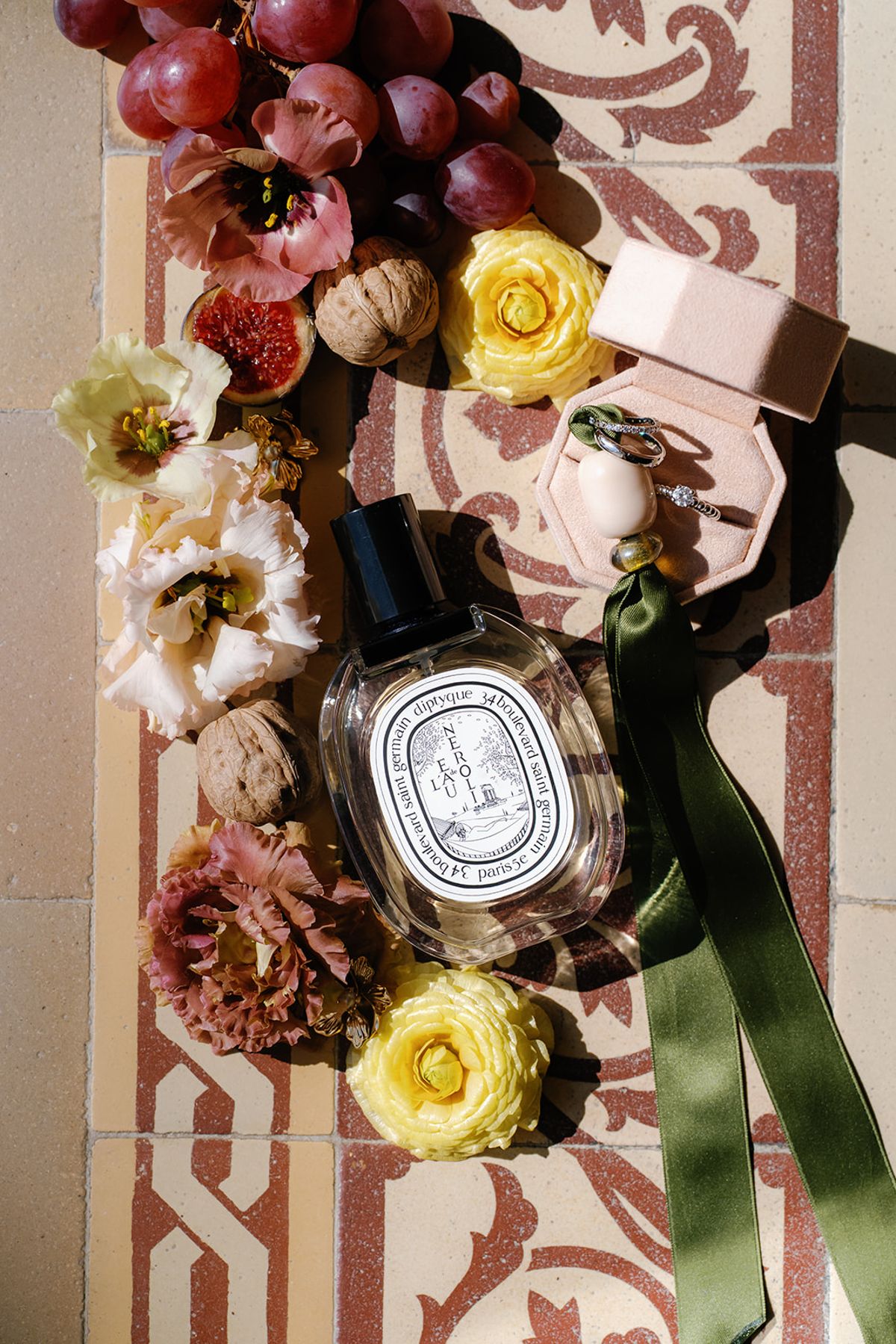 A flat lay of perfume, autumn fruit and garden flowers on patterned tile