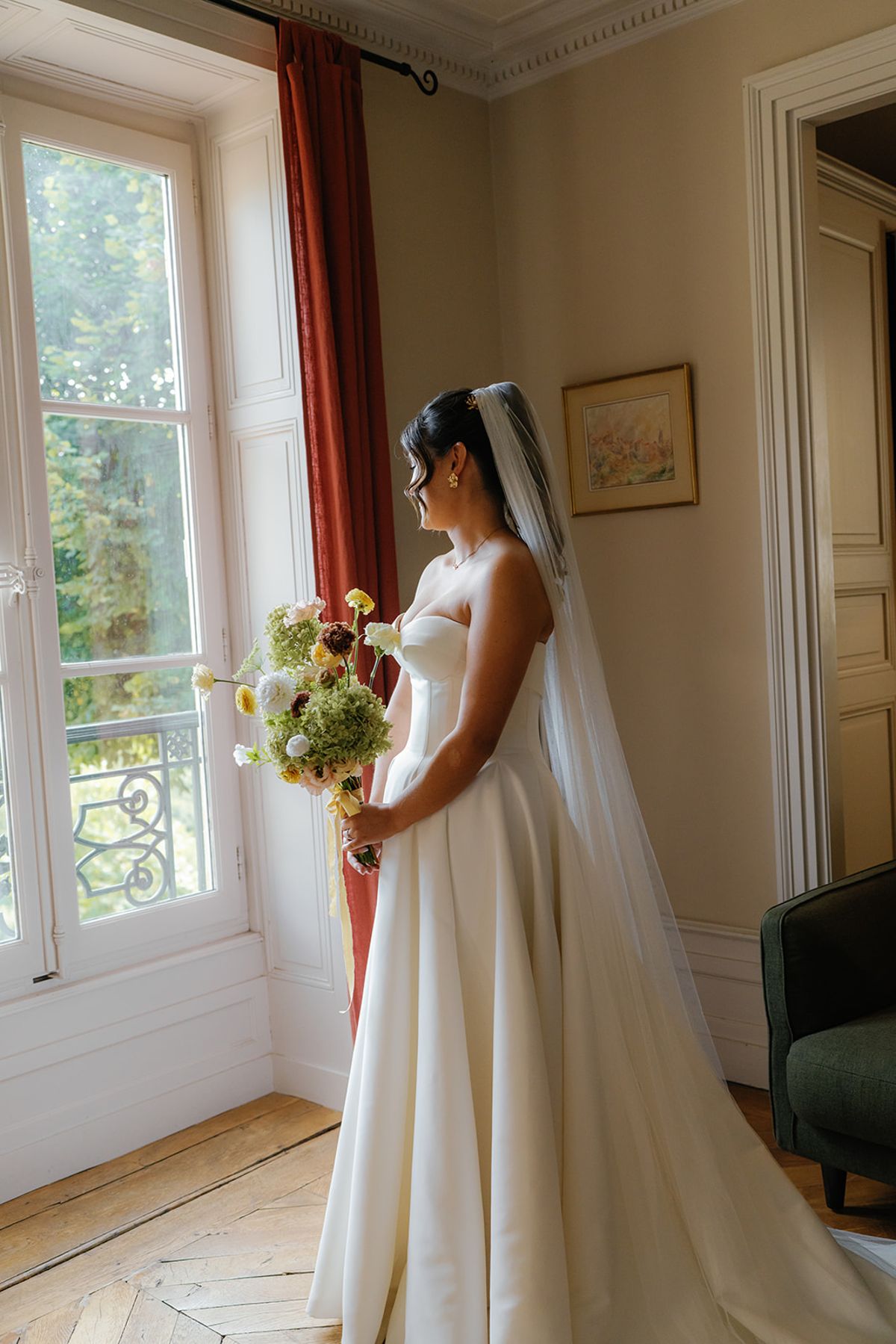 The bride at a tall window, veil falling behind her