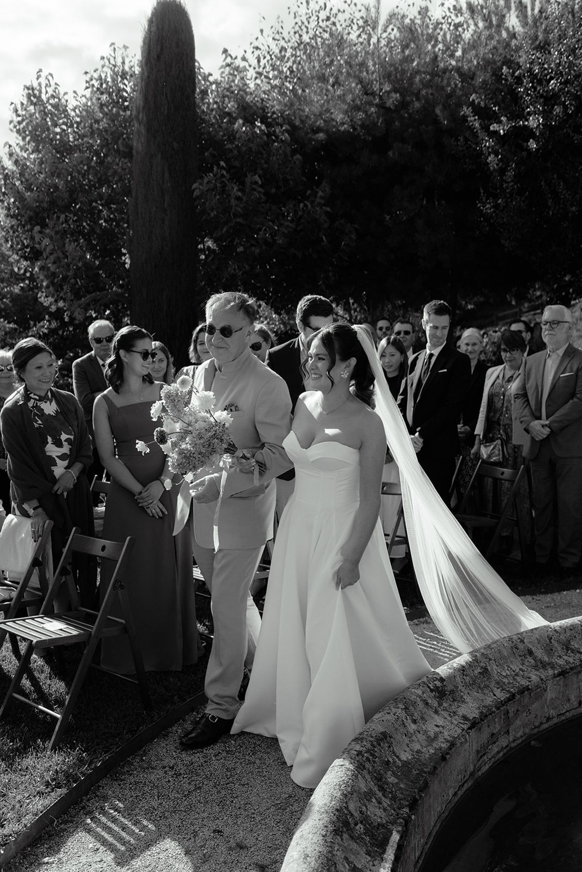 The bride walking through the seated guests in black and white
