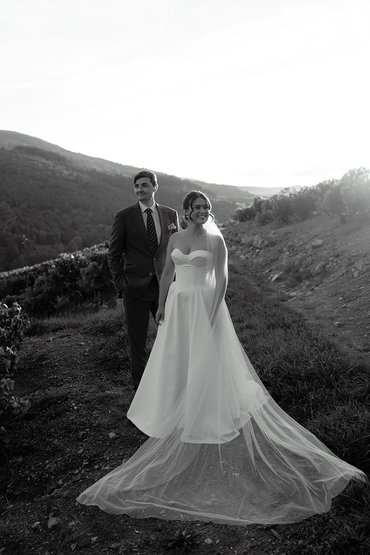 Claire and Baptiste on the hillside in black and white, the bride's train spread behind her