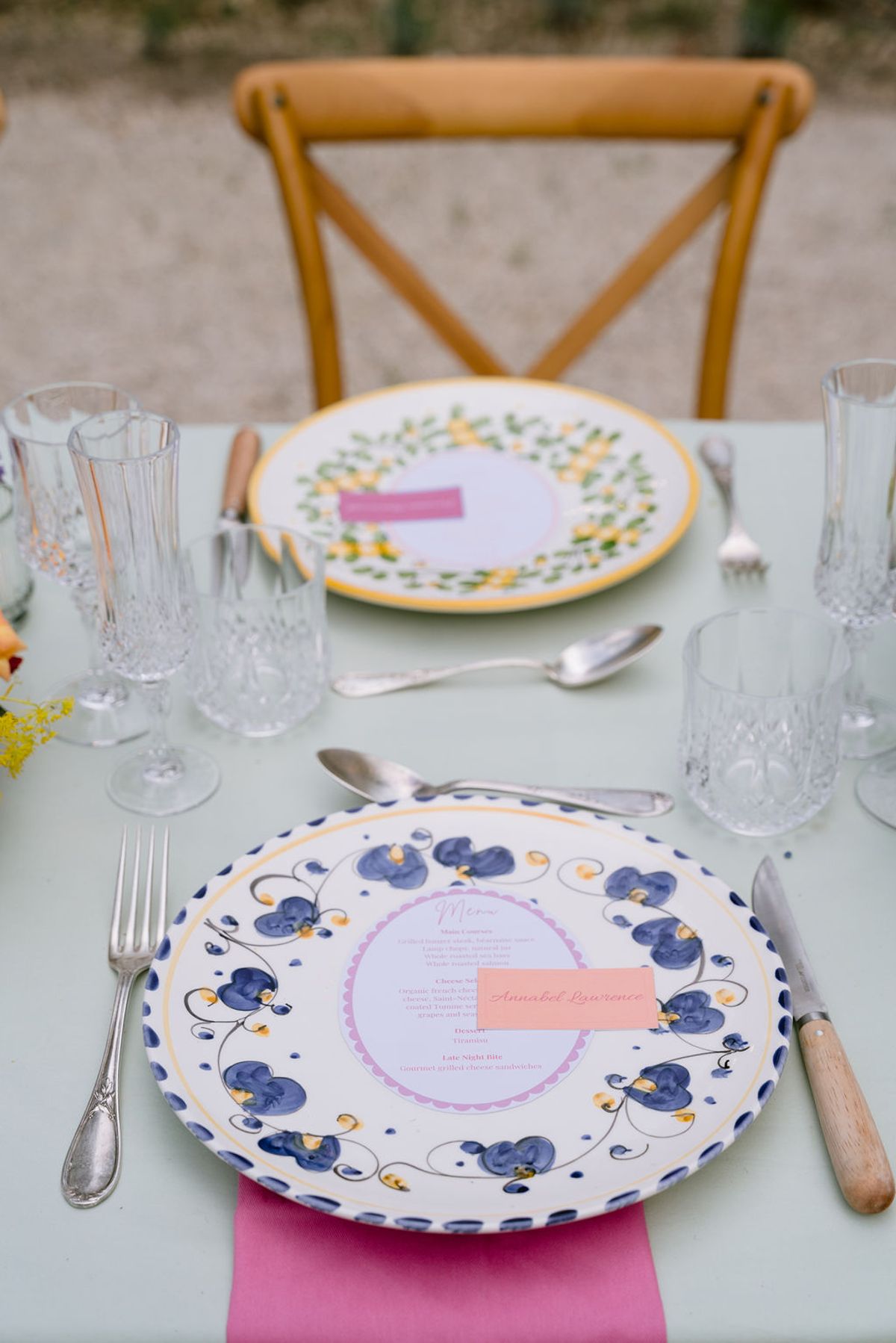 Place settings with hand-painted blue and yellow ceramic plates, menus, crystal glasses and pink napkins.