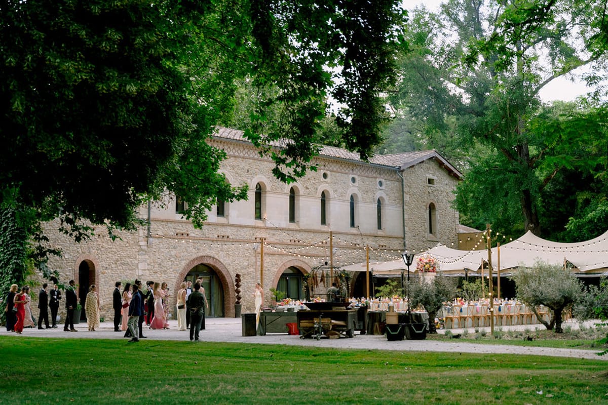 Guests gather on the lawn in front of the stone buildings of Château des Barrenques, with tables set beside tents.