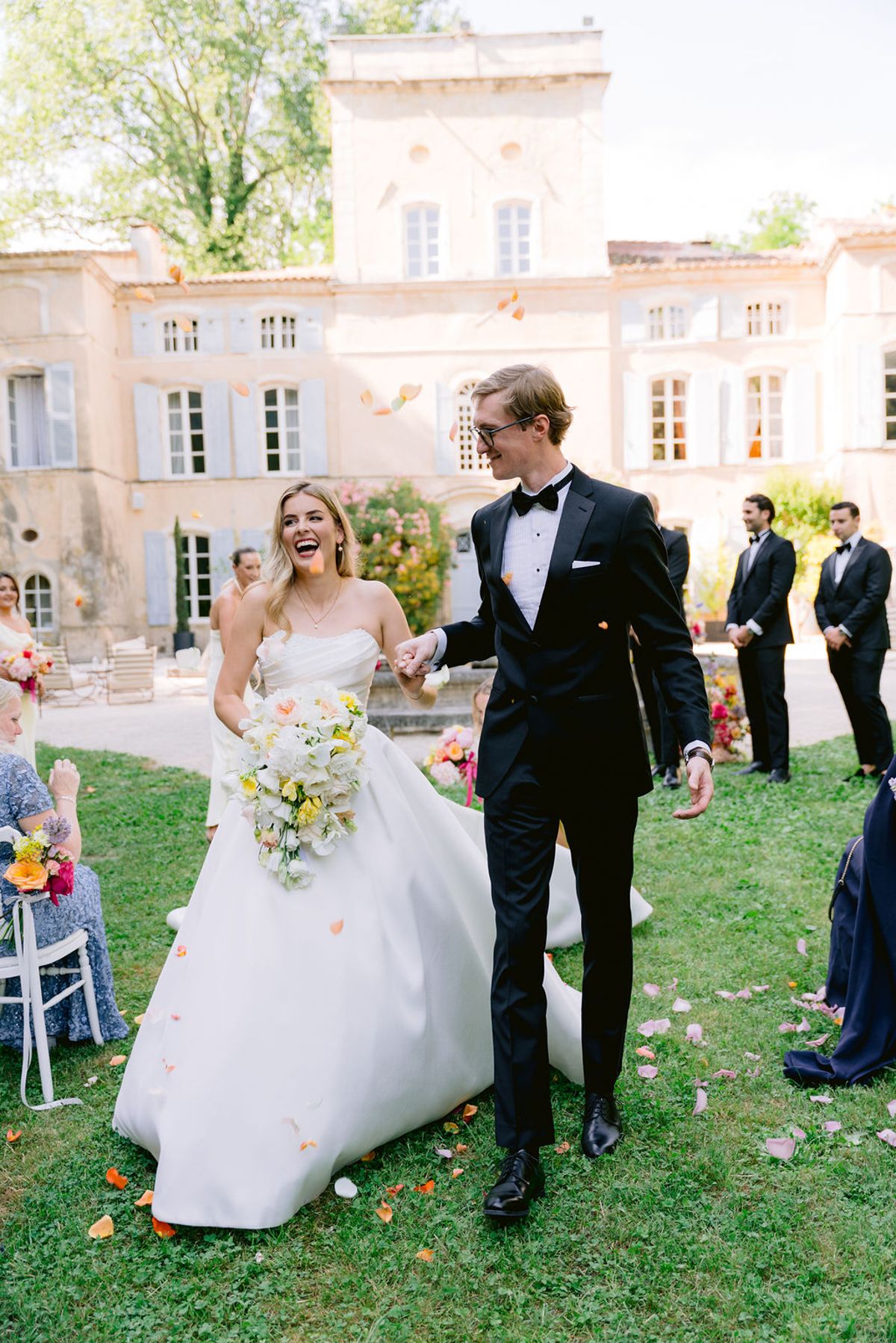 The bride and groom walk hand in hand back down the aisle as guests throw rose petals.
