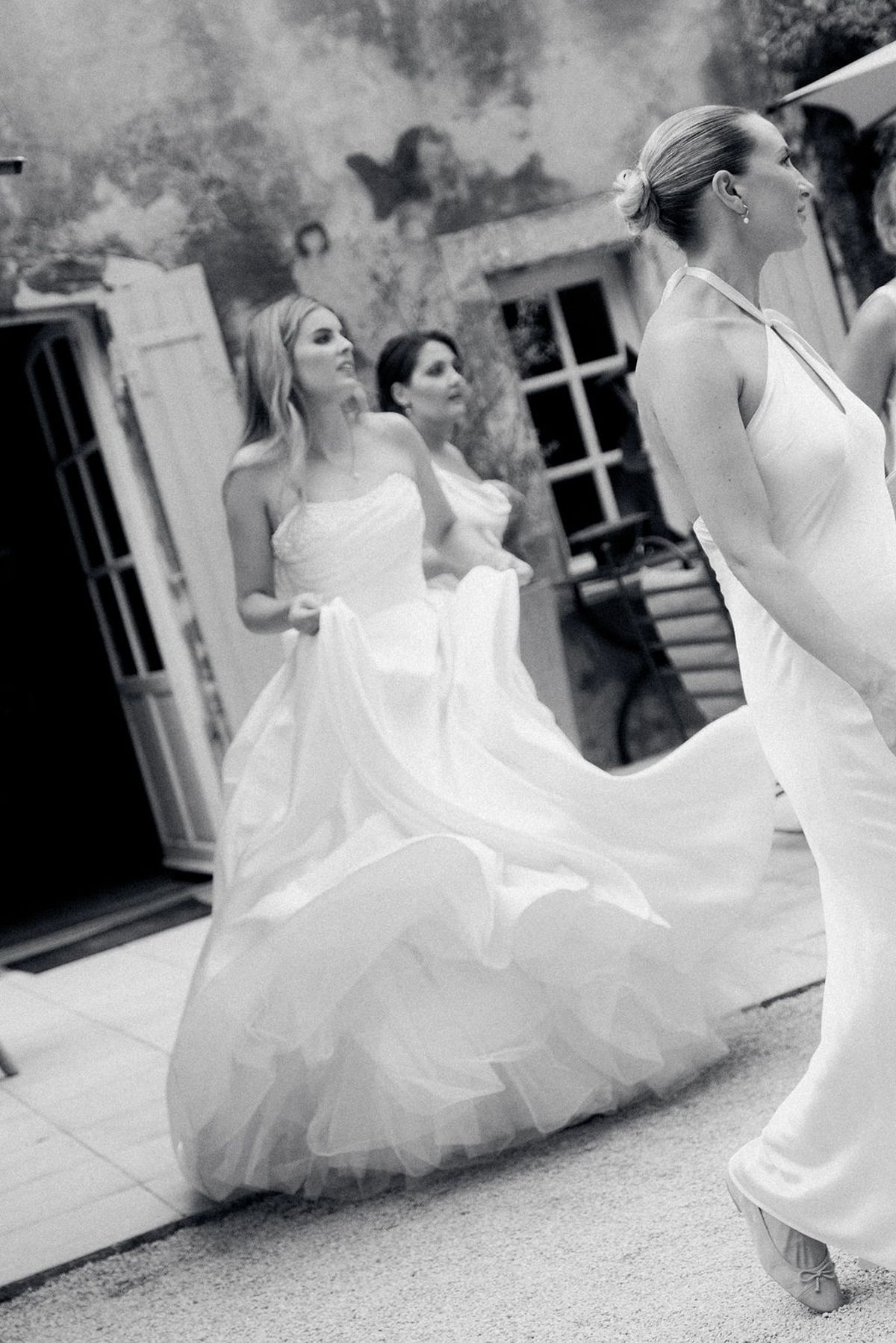 The bride lifts her full tulle skirt as she walks with her bridesmaids, in black and white.