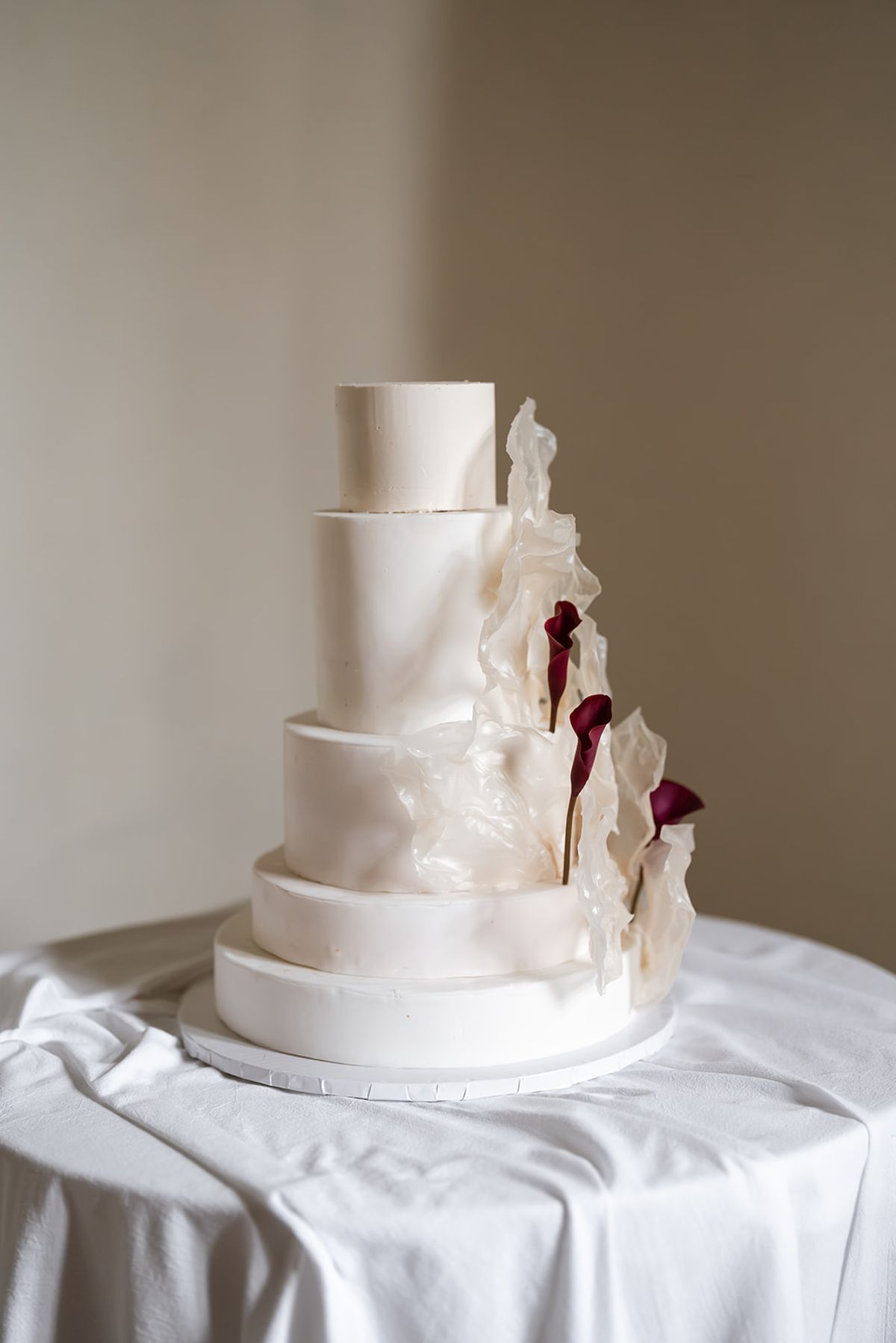 Five-tier white wedding cake with sugar petals and burgundy calla lilies
