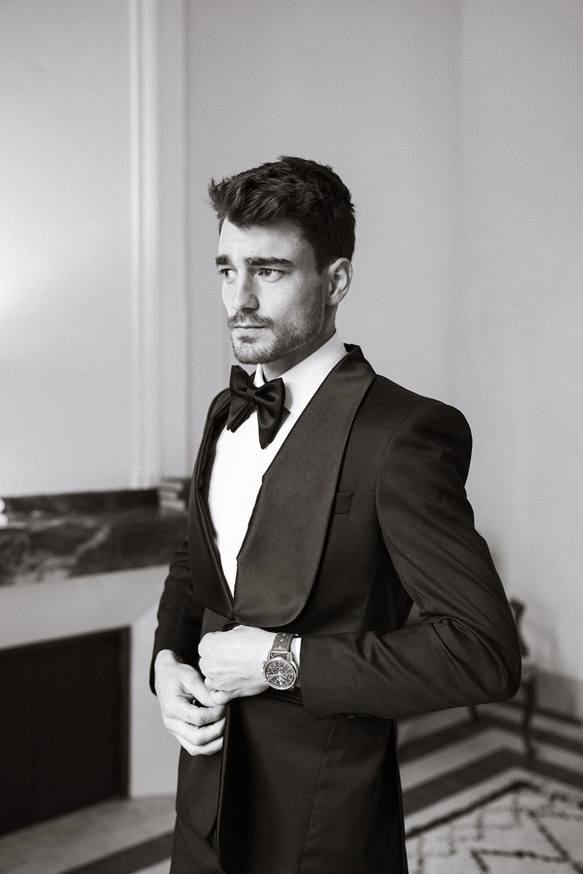 Black and white portrait of the groom in a tuxedo fastening his jacket