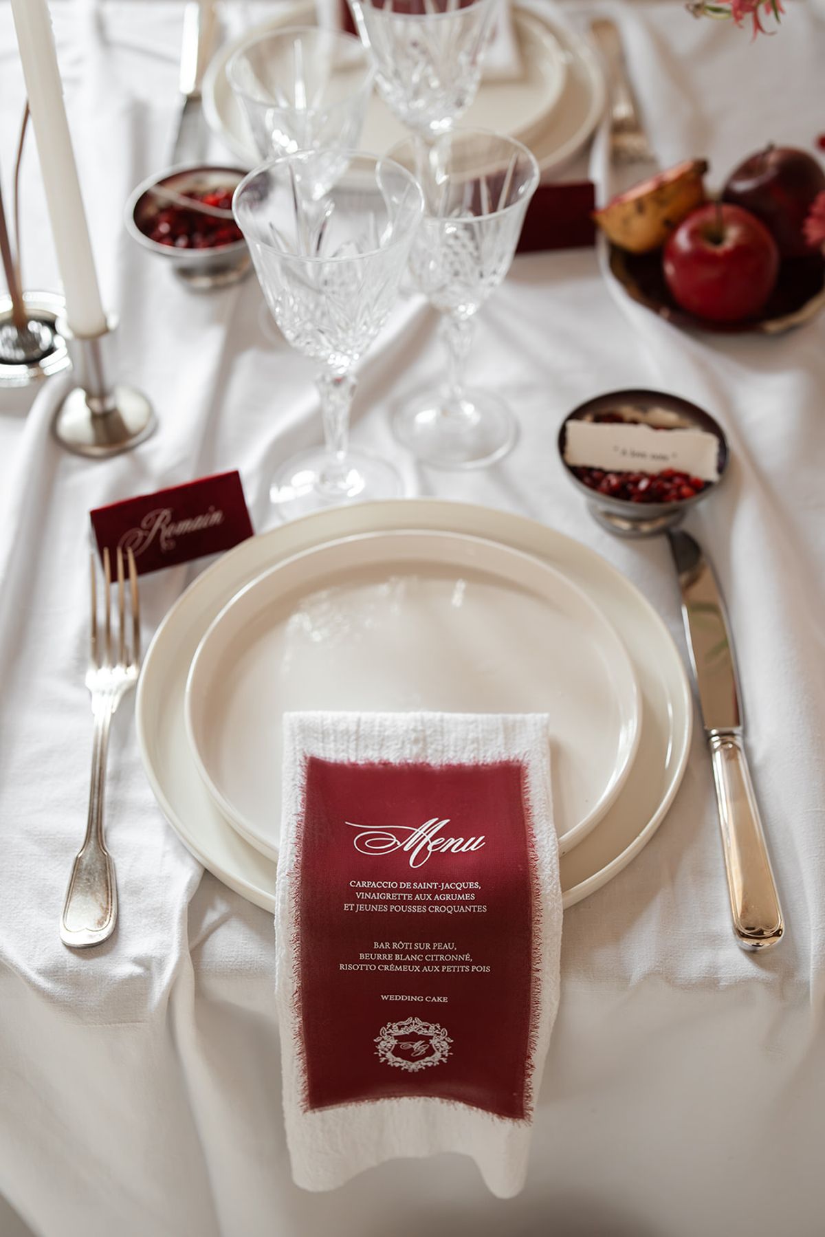 Place setting with crystal glasses, a burgundy menu card and pomegranates