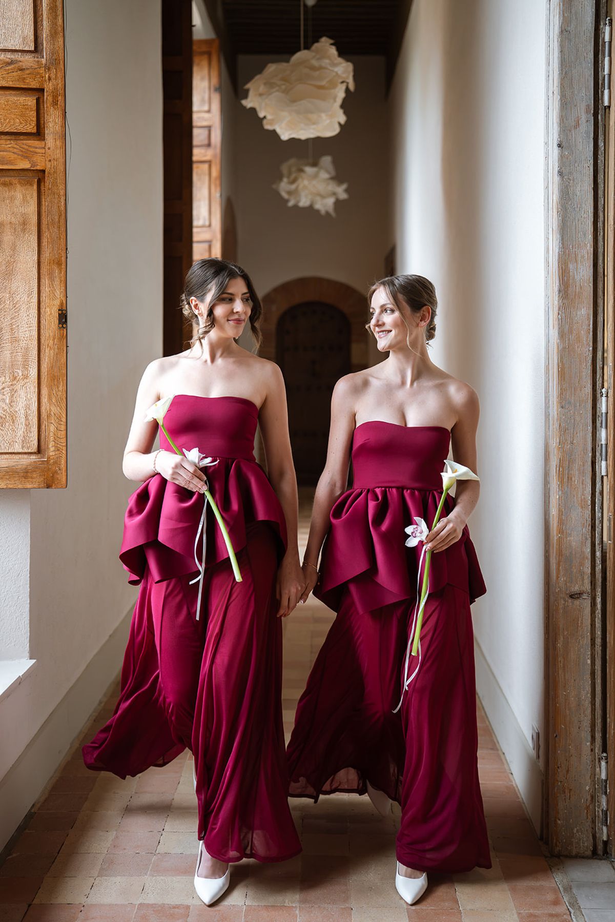 Two bridesmaids in burgundy gowns walking along a château gallery