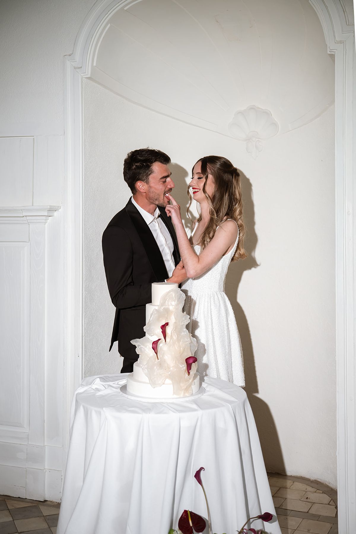 Bride and groom laughing beside the white tiered wedding cake