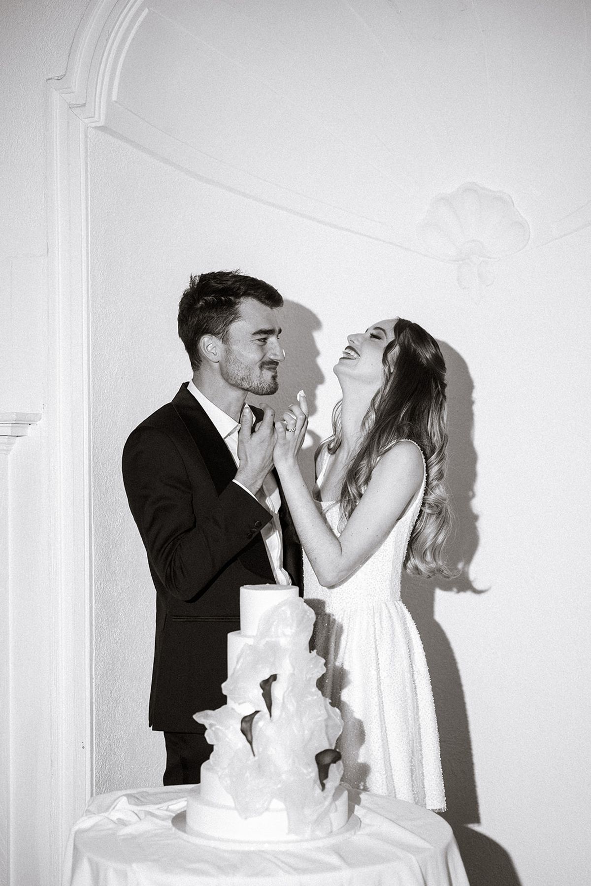 Black and white photo of the bride and groom laughing at the cake