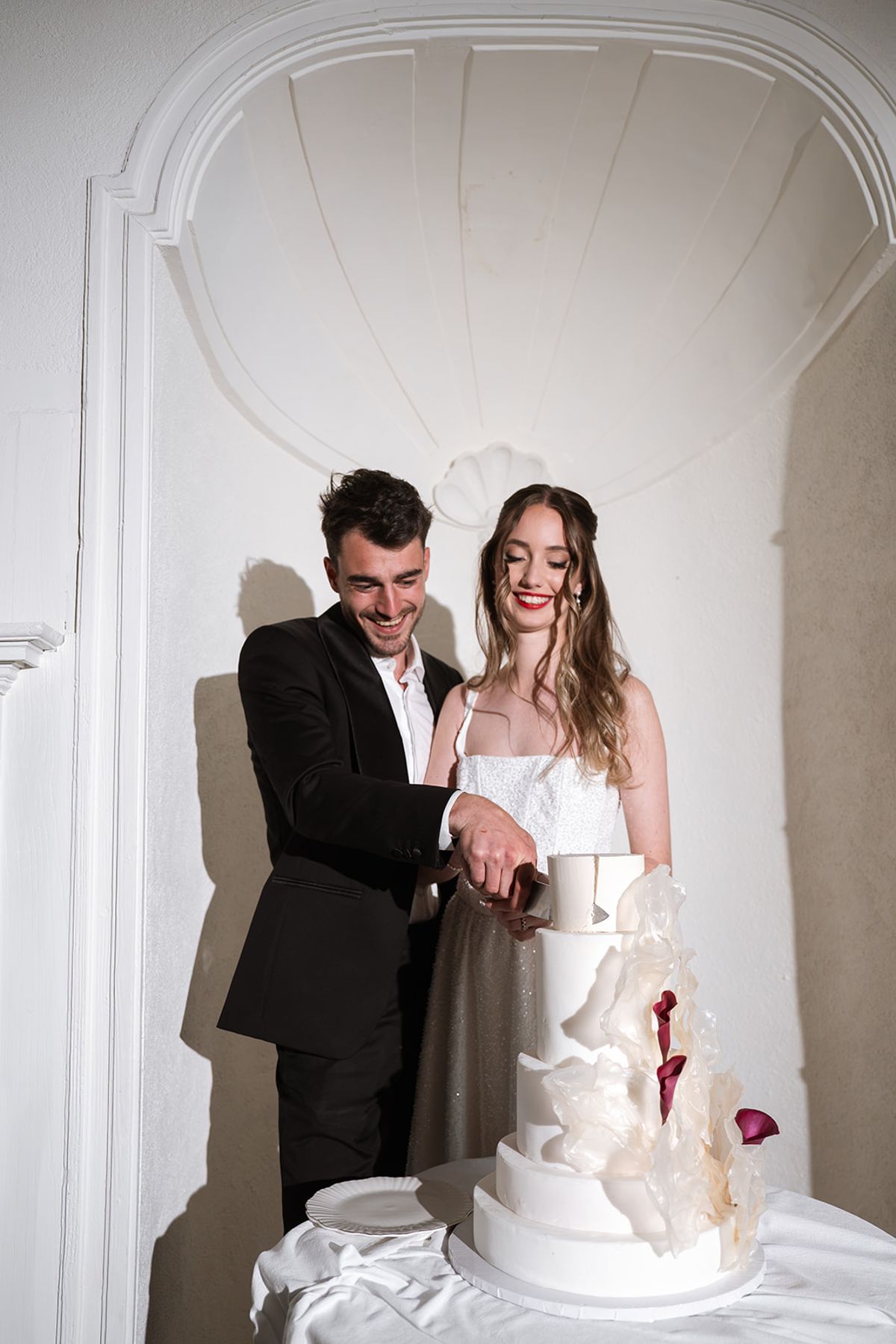 Bride and groom cutting a white tiered cake in an alcove at Château de Savignac-Mona
