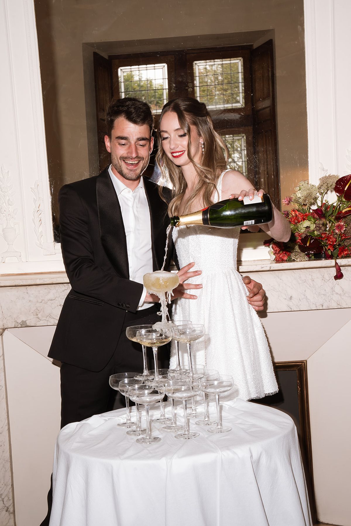 Bride pouring champagne into a champagne tower beside the groom