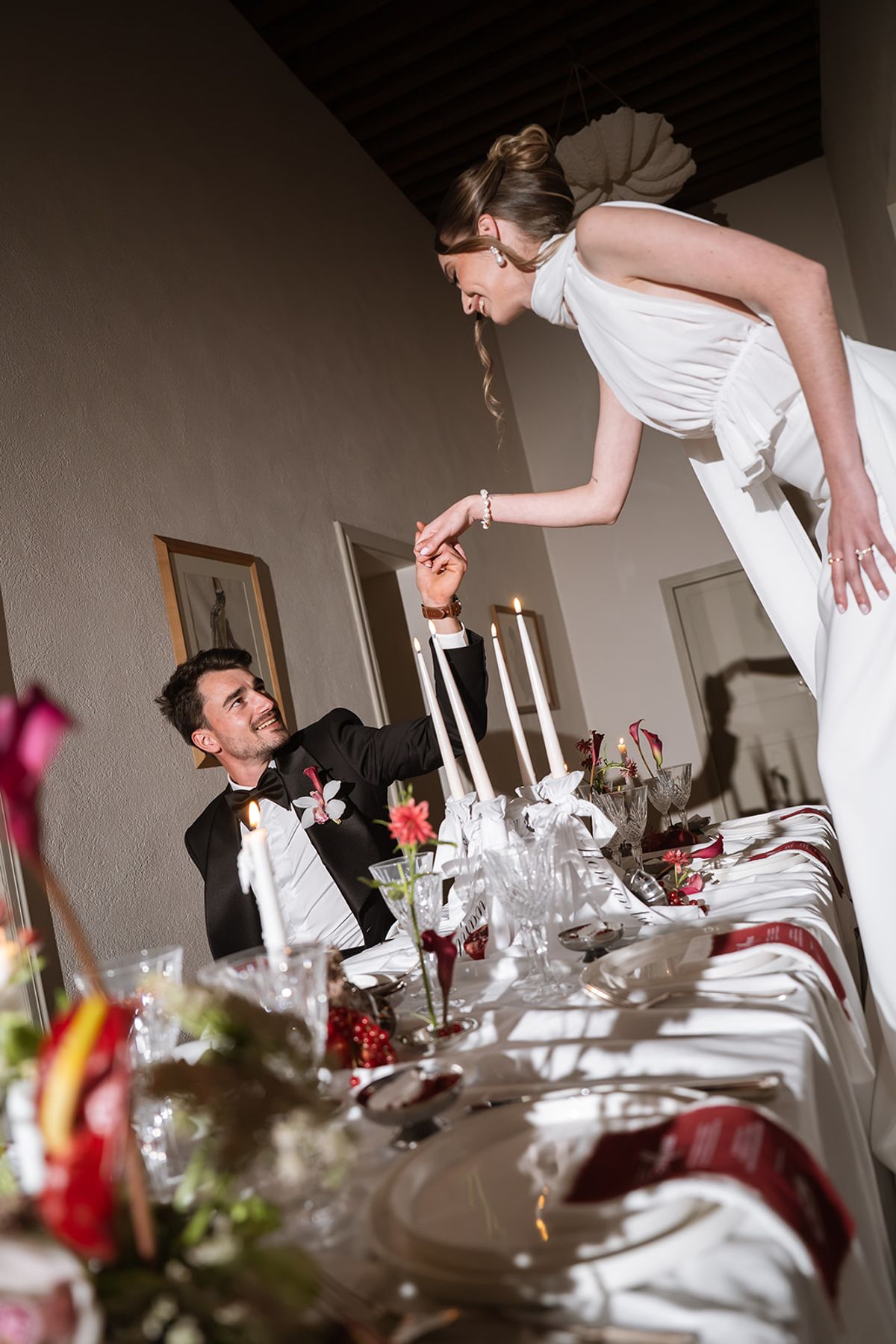 Bride leaning across the dinner table to take the groom by the hand