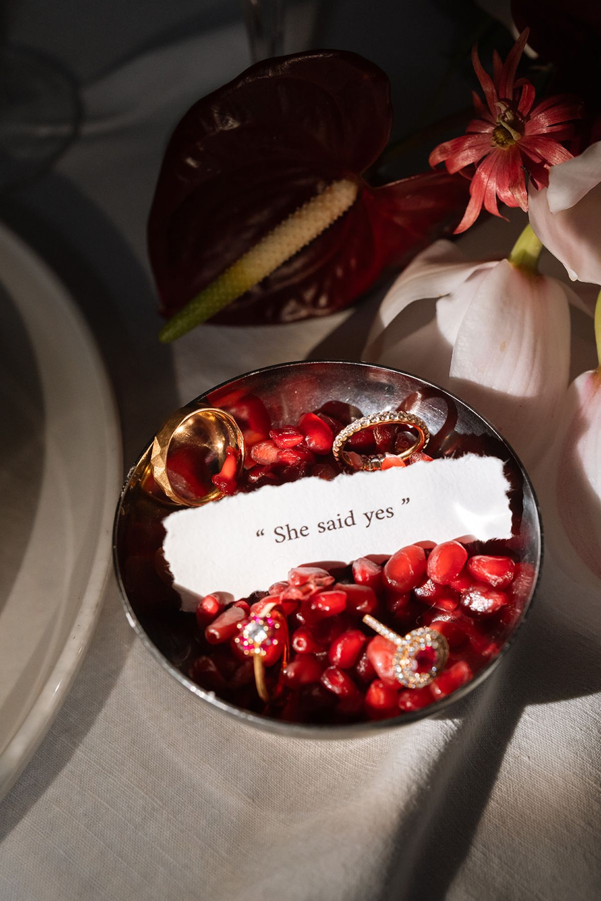 Wedding rings resting in a bowl of pomegranate seeds with a She said yes note