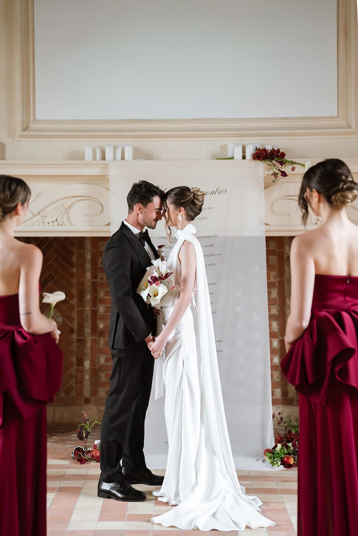 Bride and groom touching foreheads at the ceremony, flanked by bridesmaids in burgundy