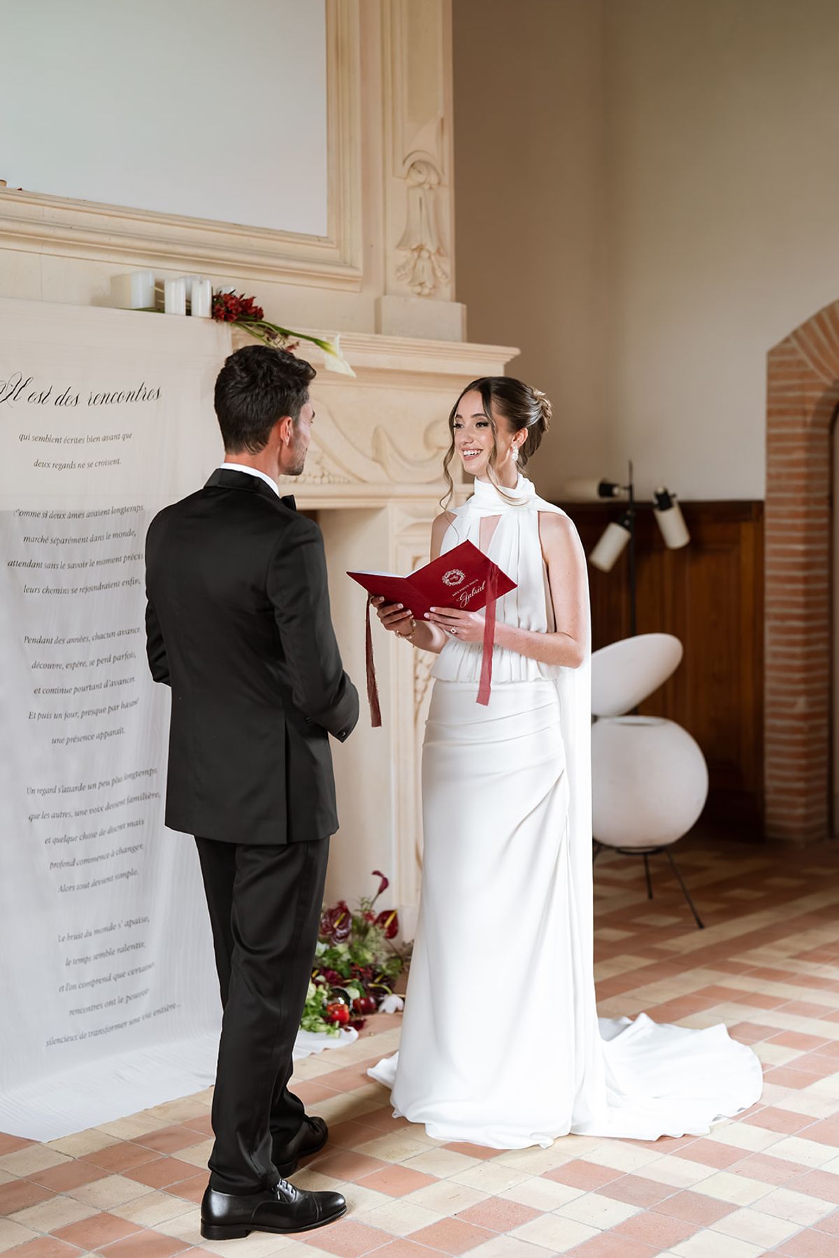 Bride and groom reading vows from burgundy booklets in a salon at Château de Savignac-Mona