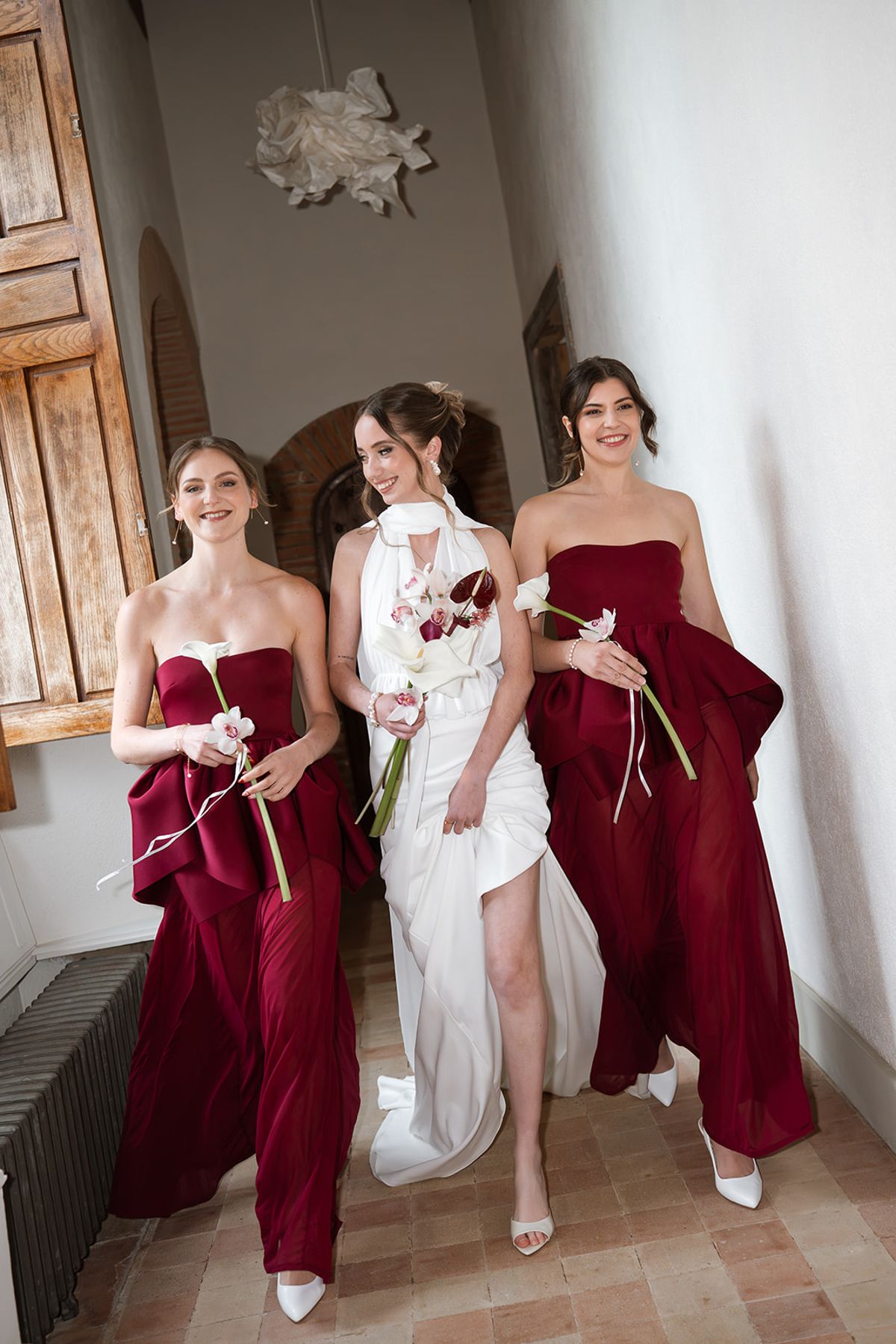 Bride walking with two bridesmaids in burgundy along a château gallery