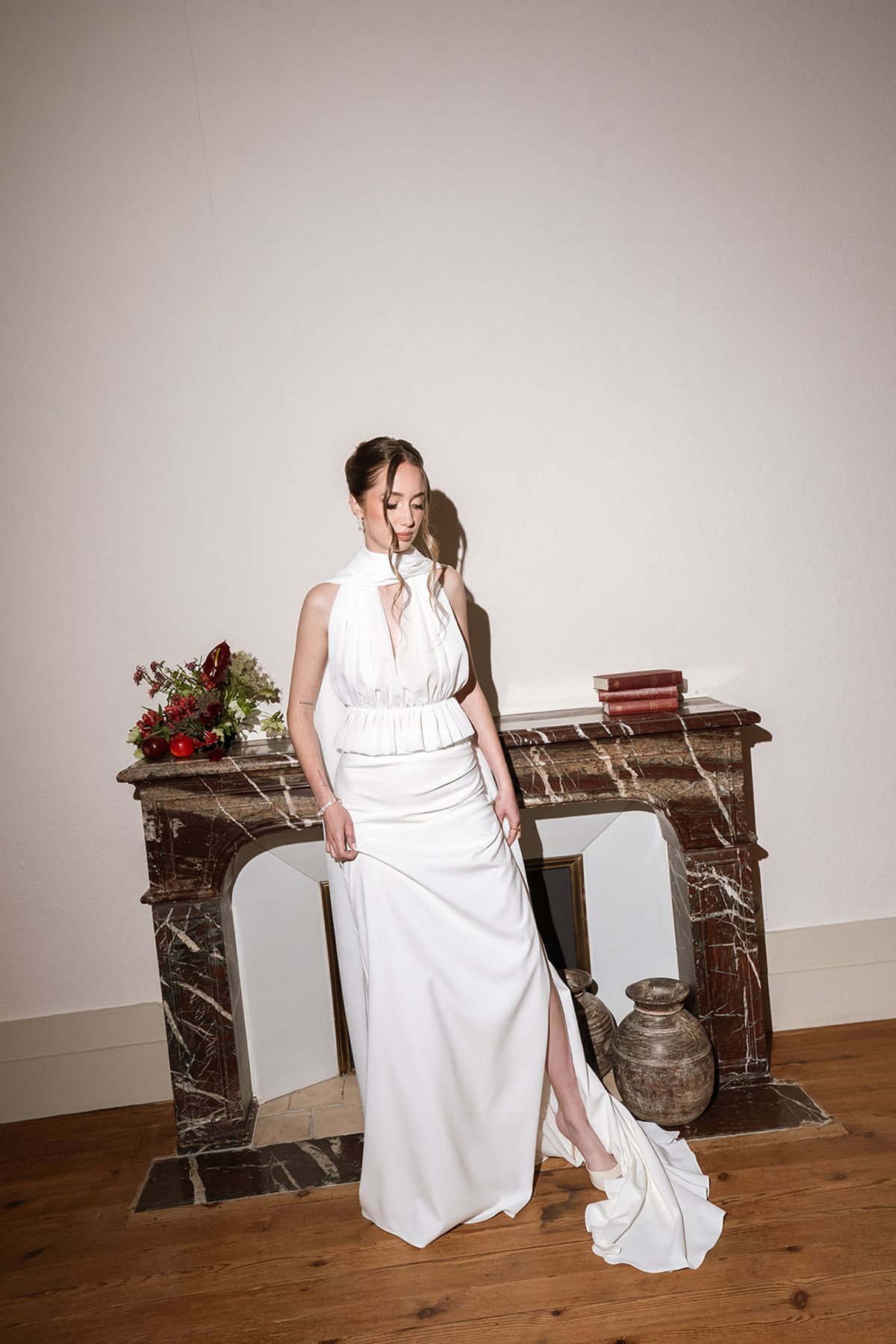 Bride in a halter-neck gown standing by a marble fireplace
